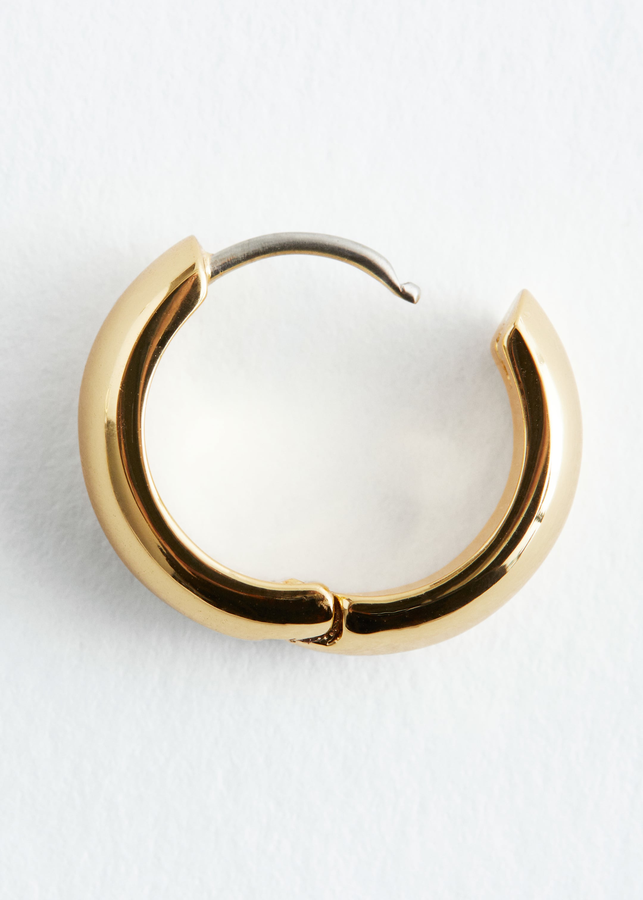 Grösseres Bild ansehen: Ein einzelner klobiger, goldfarbener Creolen-Ohrring wird aus der Seitenansicht präsentiert und zeichnet sich durch ein hochglänzendes Finish aus. Der Ohrring ist oben leicht geöffnet und zeigt einen silberfarbenen Stift, der von einer Seite ausgeht und bereit ist, sich mit der anderen zu verbinden.