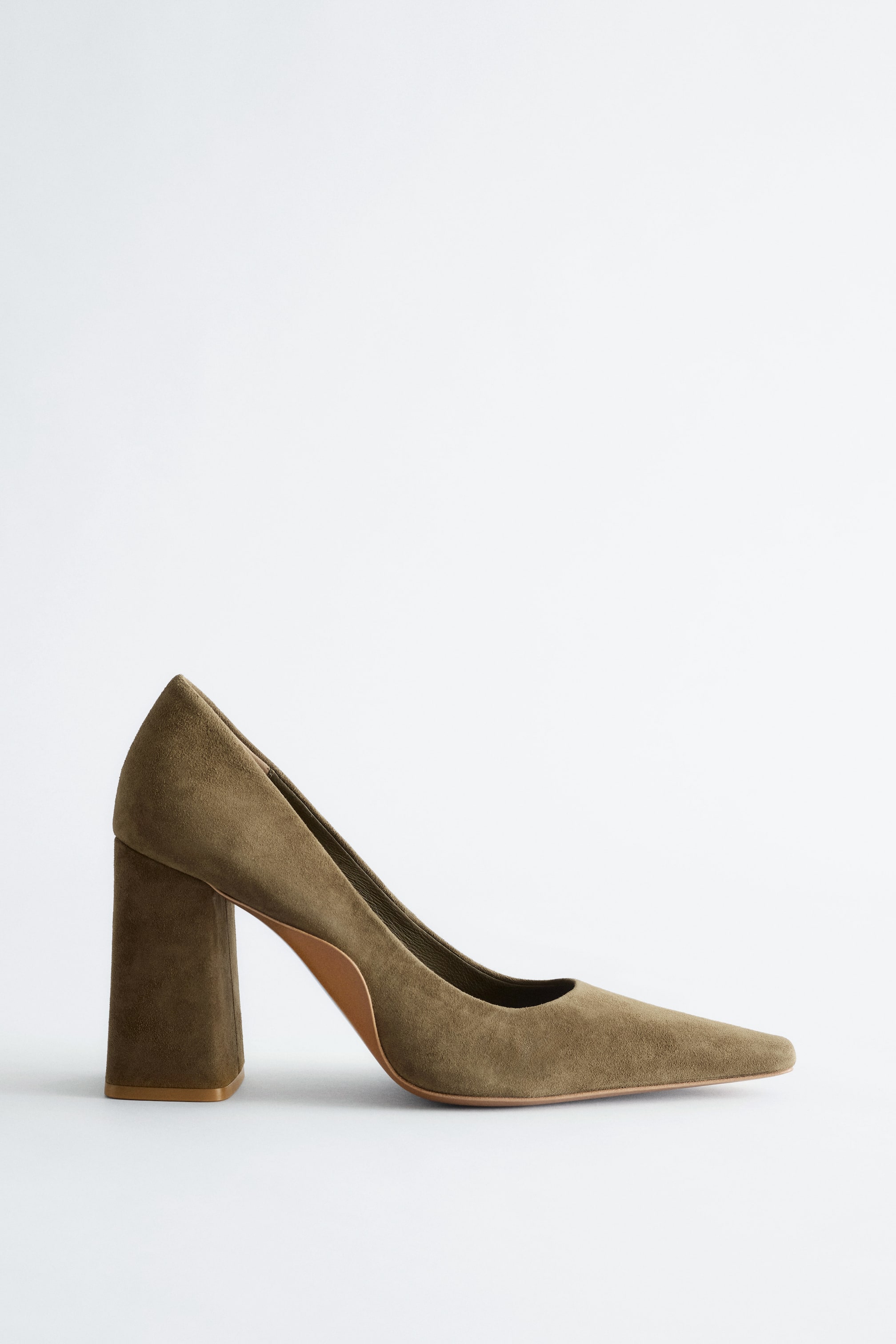View larger image: An olive green suede court shoe, positioned facing left, features a pointed toe, a lightly flared block heel, and a natural-toned sole subtly visible along the arch.