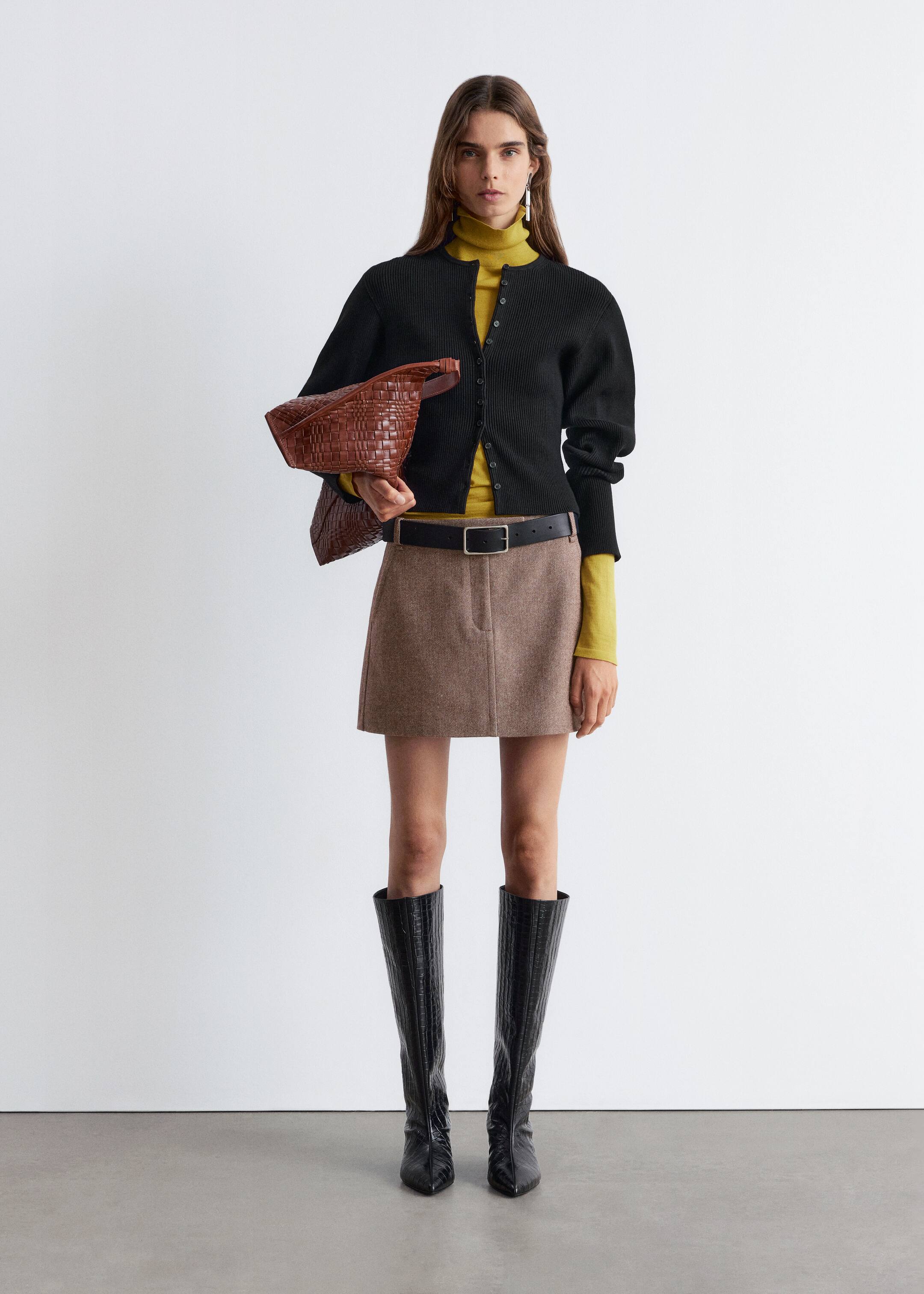View larger image: A black cardigan is being displayed front-facing, exhibiting fine vertical ribbing and a round neckline. It is styled with long, slightly puffed sleeves and a full front button closure, layering over a yellow turtleneck.