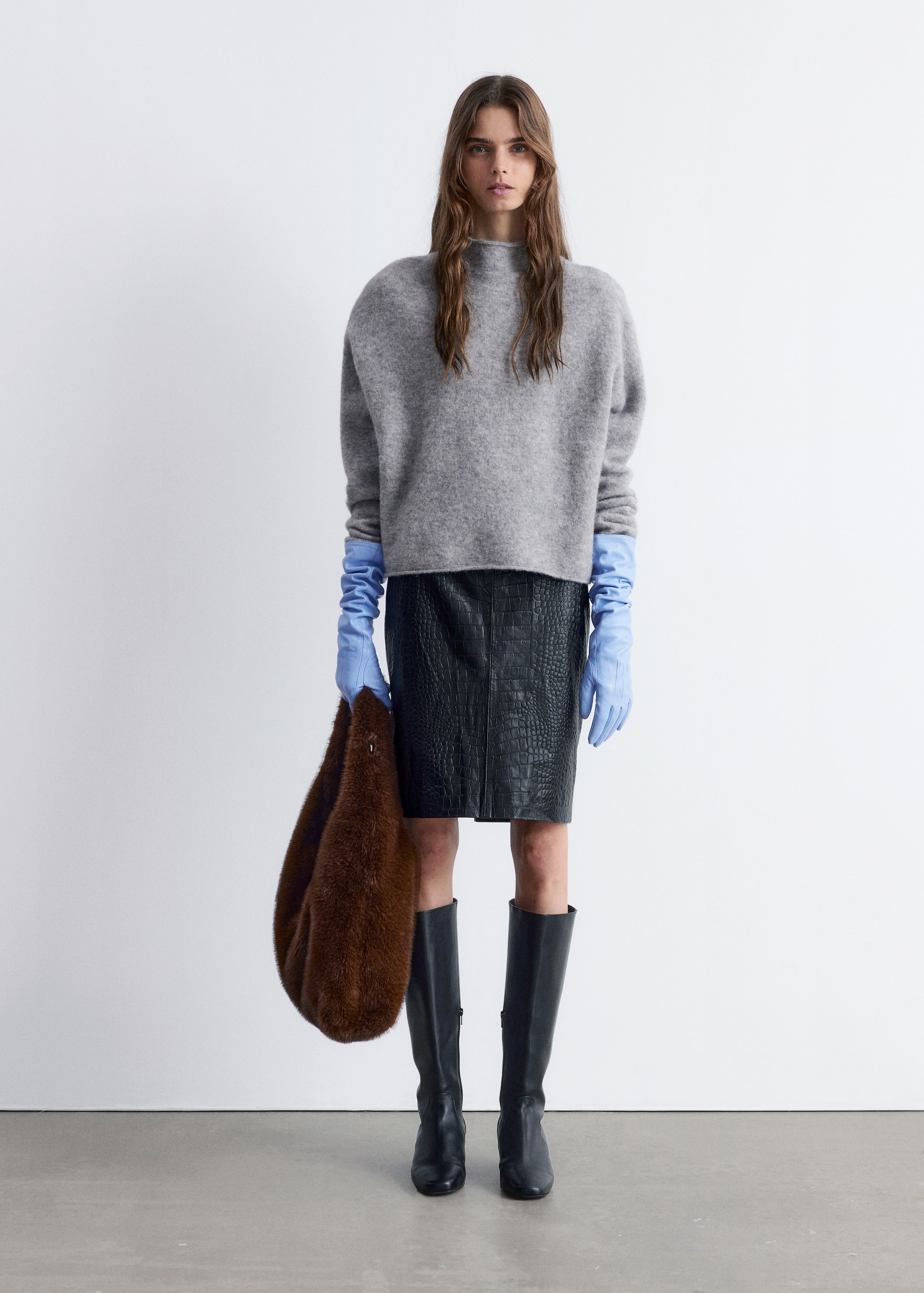 Visa större bild: En grå, mock neck-tröja visas upp, med en avslappnad, oversized passform och nedhasade axlar. Dess långa ärmar sträcker sig över ljusblå handskar och avslöjar en mjuk, luddig textur.