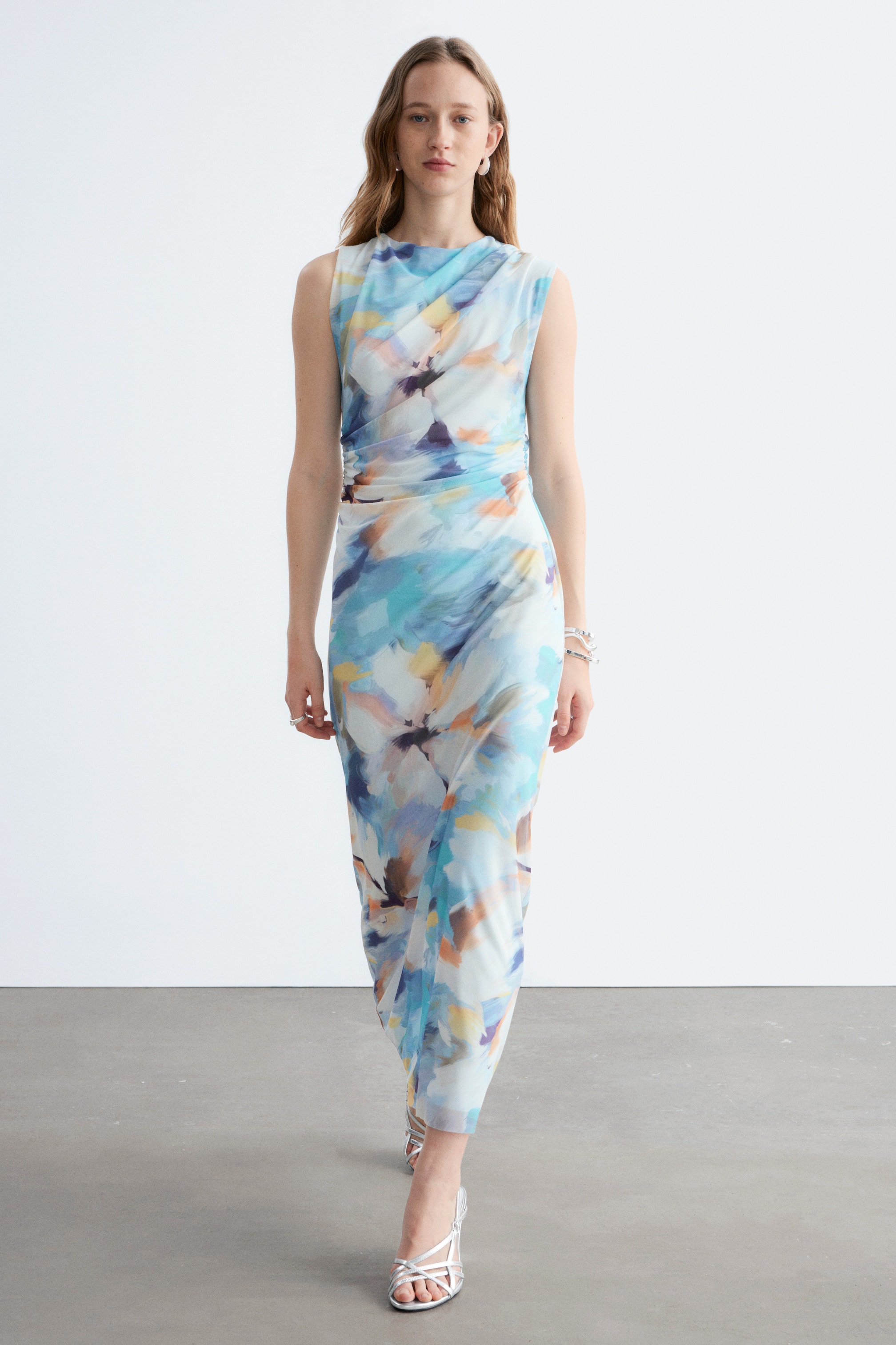Größeres Bild anzeigen: Das ärmellose Kleid präsentiert ein abstraktes Aquarellmuster in Blau-, Türkis-, Orange- und Brauntönen, mit einem drapierten Ausschnitt und gerafften Details an der Taille. Es fließt bis zu einem knöchellangen Saum hinunter.