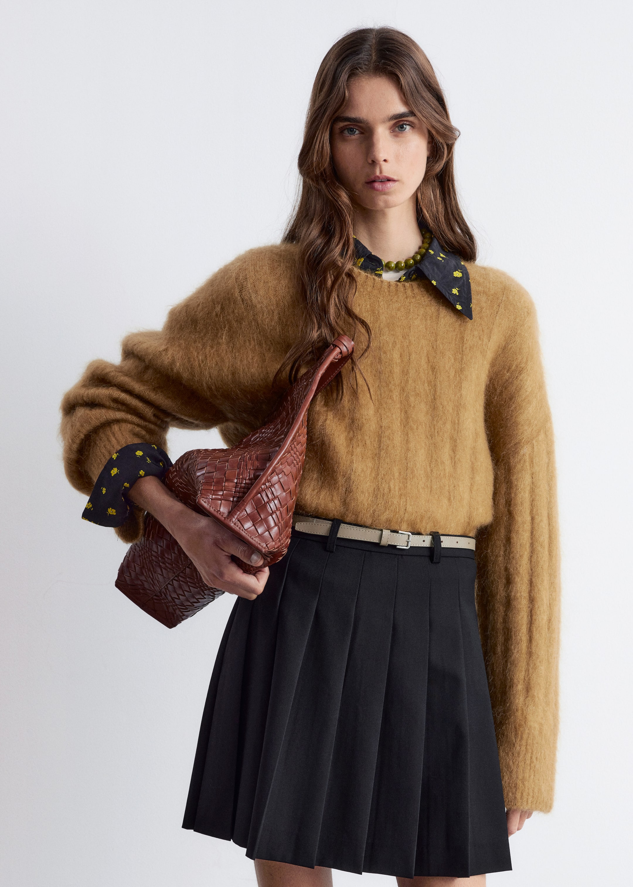 Agrandir l'image: Un pull à col rond marron et duveteux est porté, avec une coupe ample et des manches longues. Une chemise noire avec un motif floral jaune dépasse sous son col et ses poignets, superposée avec un collier de perles vertes.