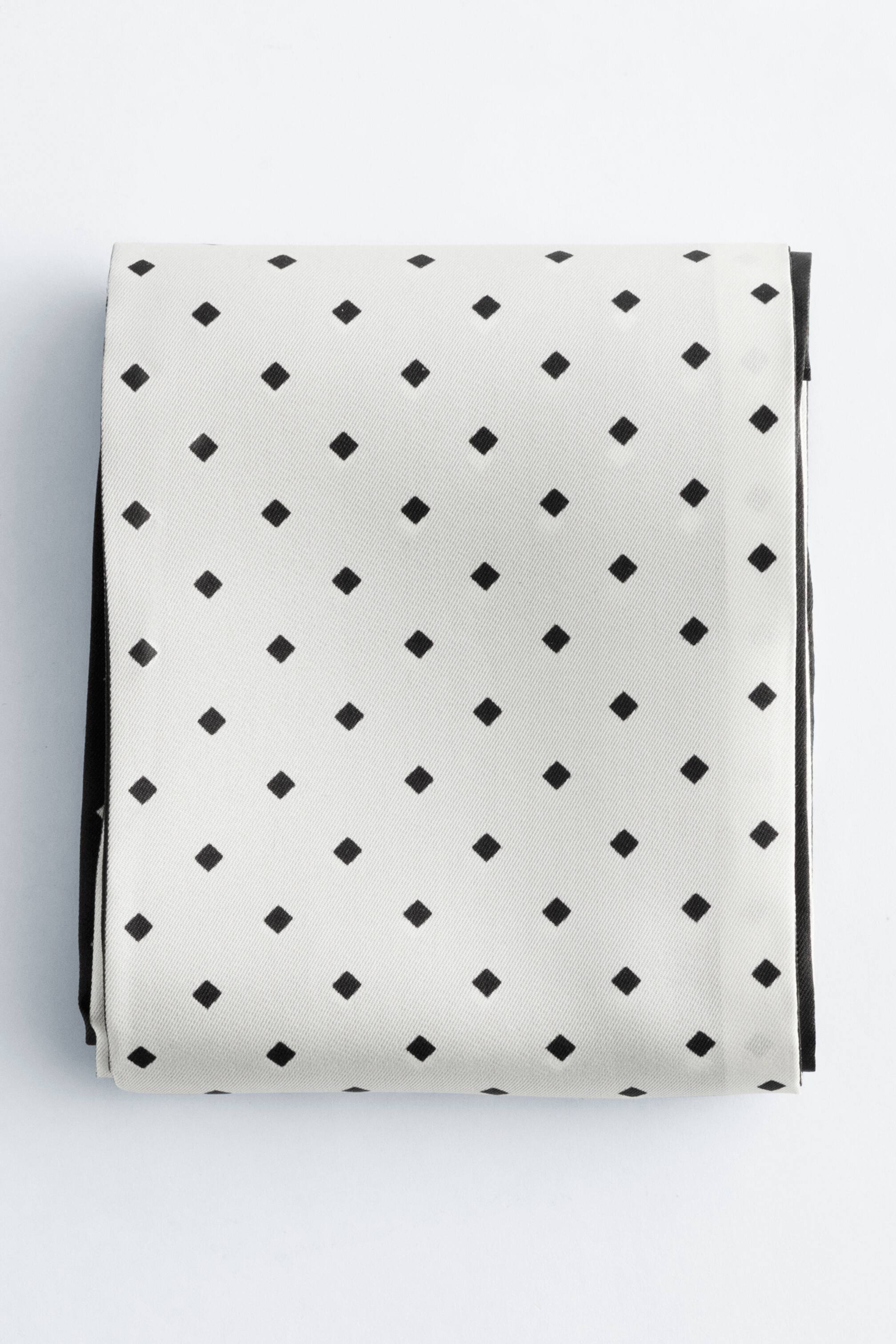 Visa större bild: Produkten är en vikt näsduk, som visar en ljus krämfärg mönstrad med jämnt fördelade svarta diamantformer. En svart kant är synlig längs den högra och nedre vikningen av tyget.