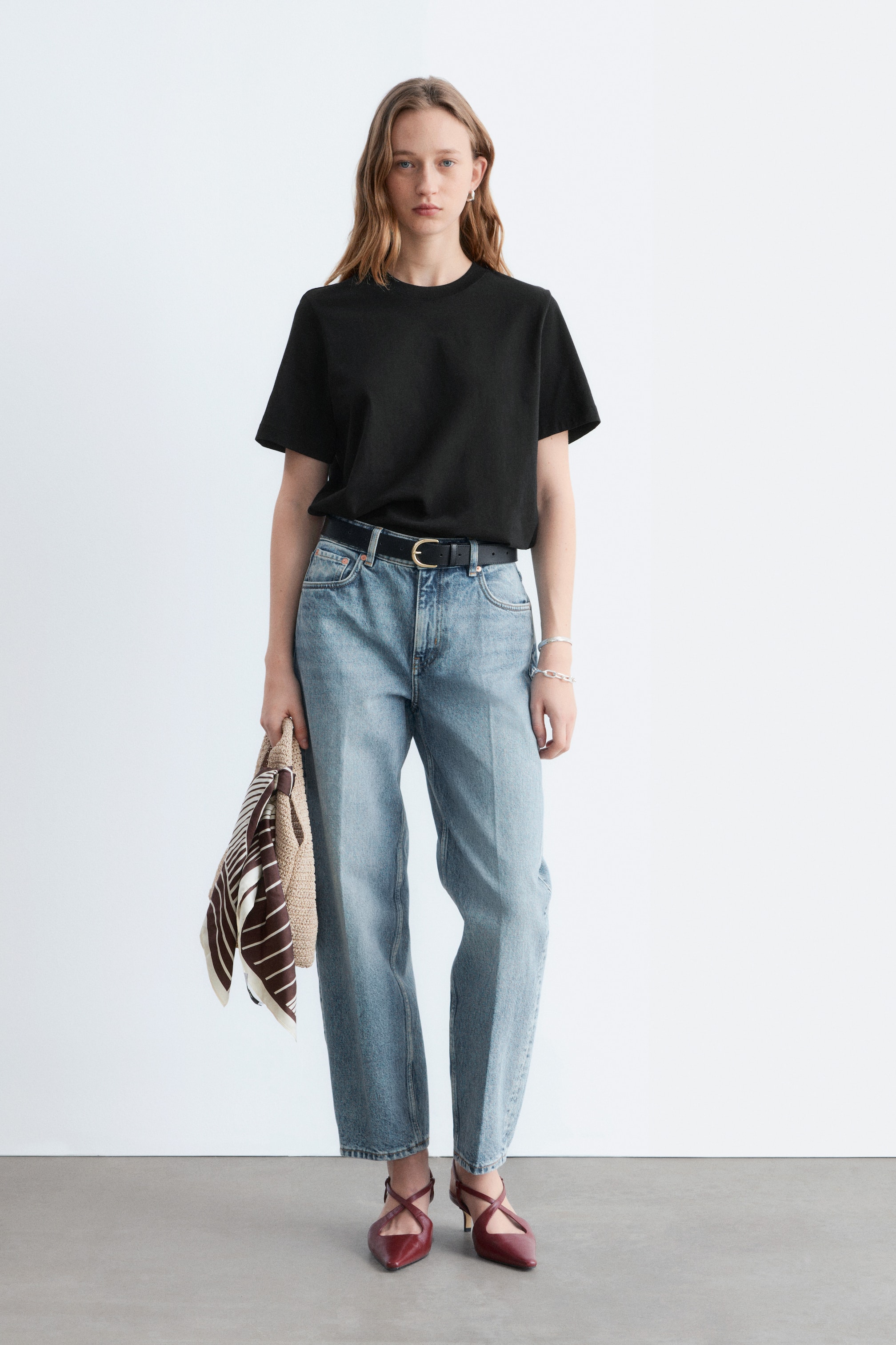 Se større billede: En sort t-shirt med afslappet pasform vender fremad, med rund hals og korte ærmer, og er stoppet ned i lyseblå jeans med et synligt sort bælte.