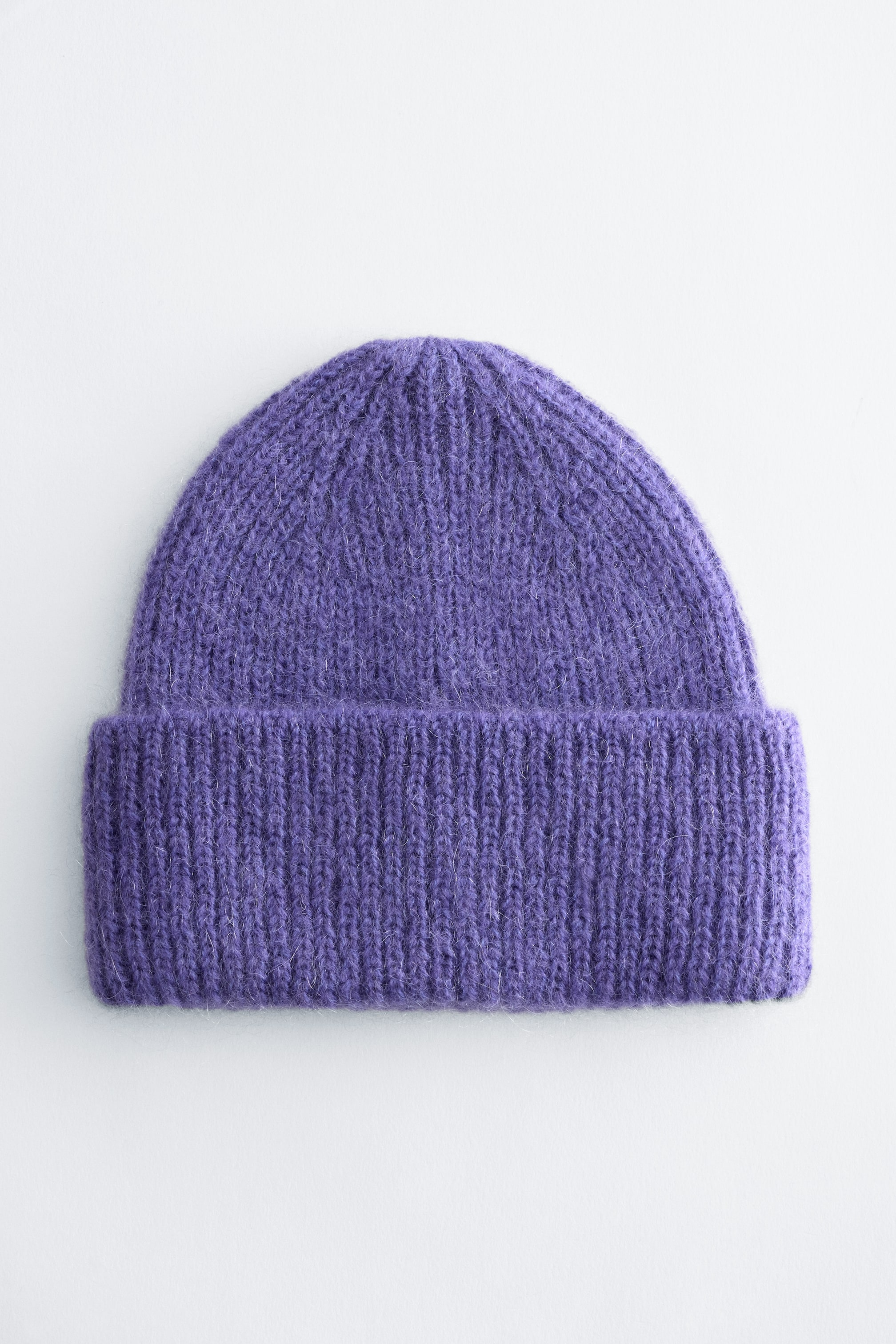 Ver imagem maior: Um gorro roxo em malha canelada é mostrado de frente, apresentando uma malha fofa e texturada e uma aba larga dobrada.
