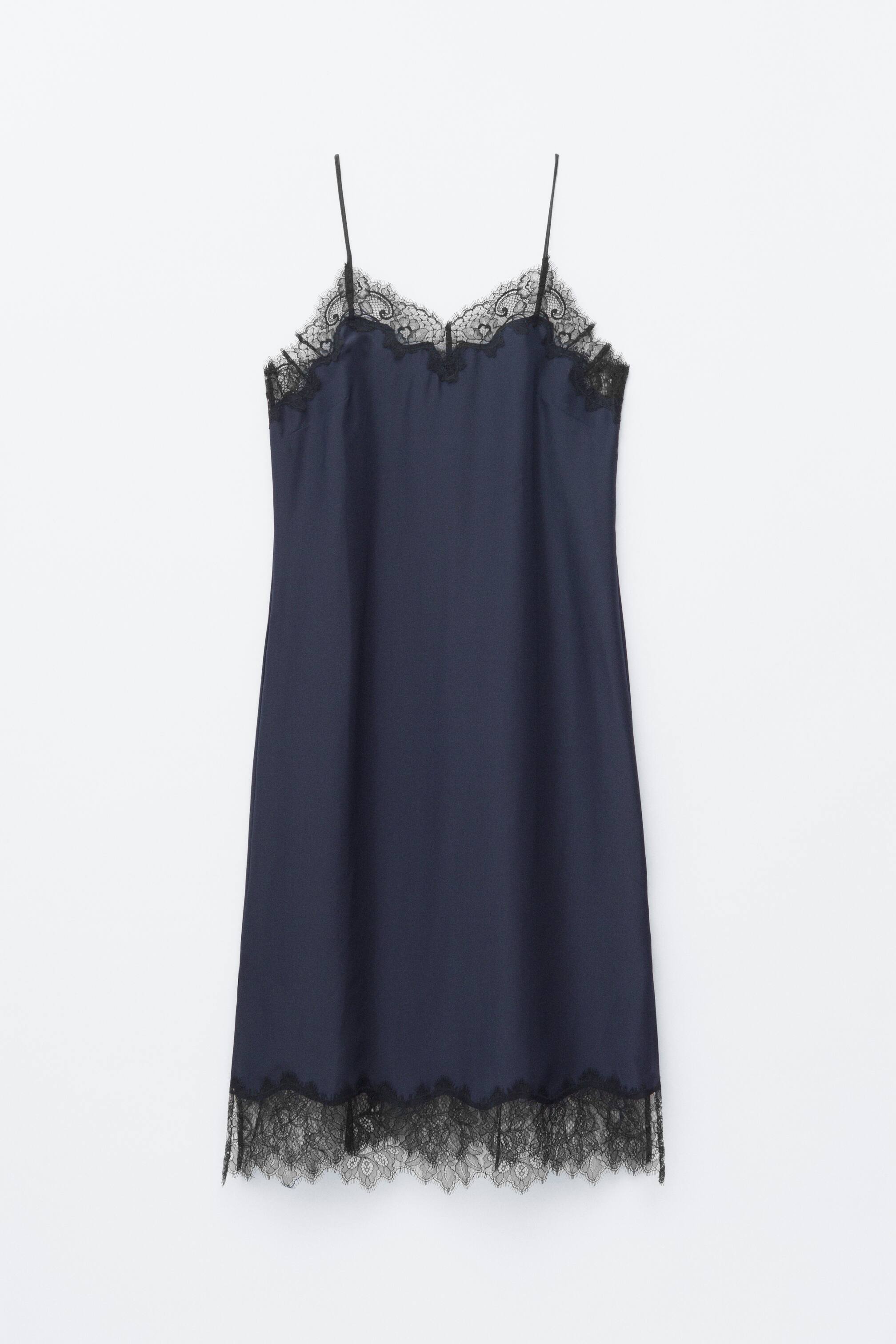 Преглед на по-голямо изображение: Тъмносиня копринена рокля тип "слип" е показана отпред, с права кройка и черна дантела, която украсява деколтето и подгъва, и тънки регулируеми презрамки тип "спагети".