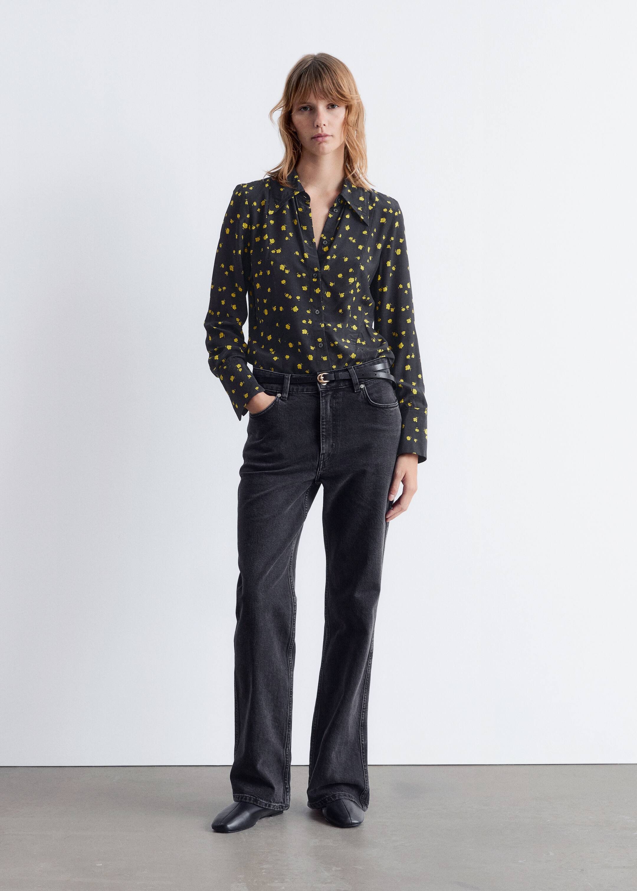 Ver imagem maior: Uma camisa preta de manga comprida com botões, estampada com pequenas formas abstratas amarelas e com uma gola clássica e punhos com botões, está a ser exibida. Está a ser combinada com jeans de cintura alta e lavagem escura, que estão a ser apertados por um cinto preto fino com uma fivela clara, e sapatos rasos de bico quadrado pretos estão a completar o conjunto.