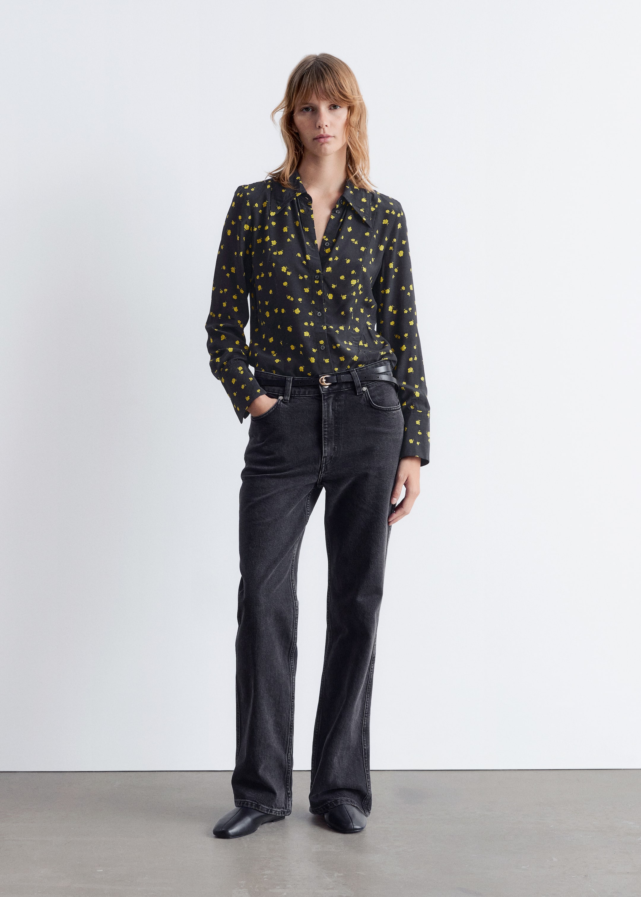 View larger image: A black long-sleeved button-up shirt, patterned with small yellow abstract shapes and featuring a classic collar and buttoned cuffs, is being shown. It is being styled with dark wash, high-waisted jeans, which are being cinched by a thin black belt with a light buckle, and black square-toe flats are completing the ensemble.