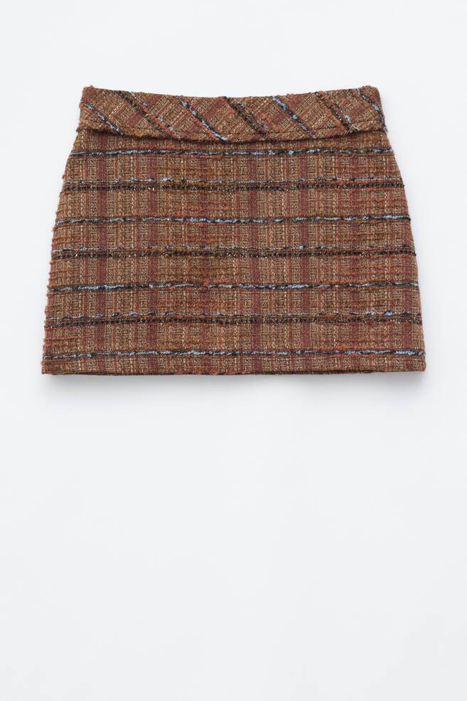 The tweed mini skirt is shown from the front, featuring a textured brown fabric with horizontal stripes in blue, black and rust. The design includes a fold-over waistband displaying a diagonal striped pattern and a structured, straight-cut silhouette. - 1