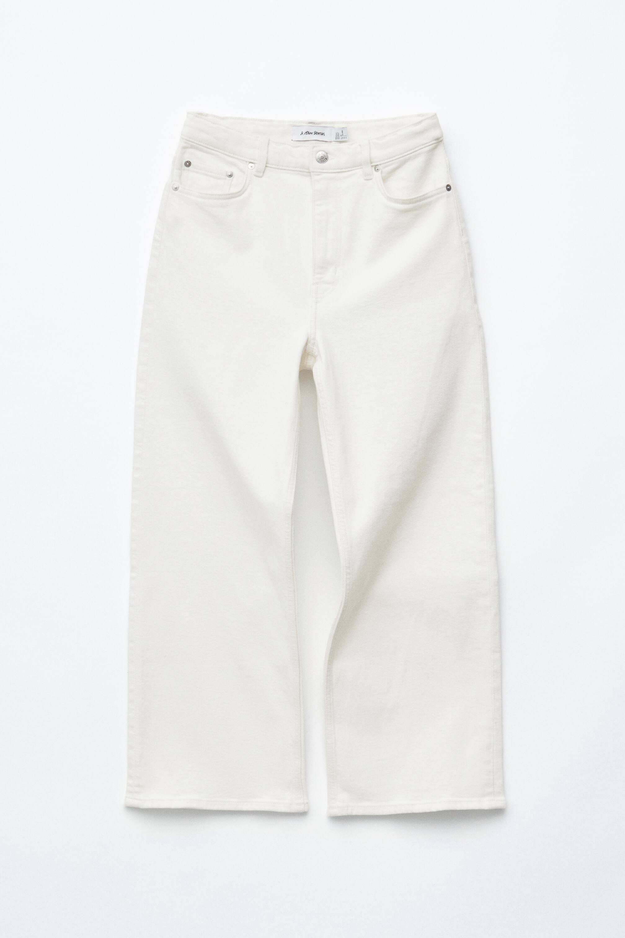 Agrandir l'image: L'AVANT du jean blanc taille haute présente un design classique à 5 poches avec une fermeture éclair et bouton, une coupe régulière, et une jambe large raccourcie se terminant à la cheville.