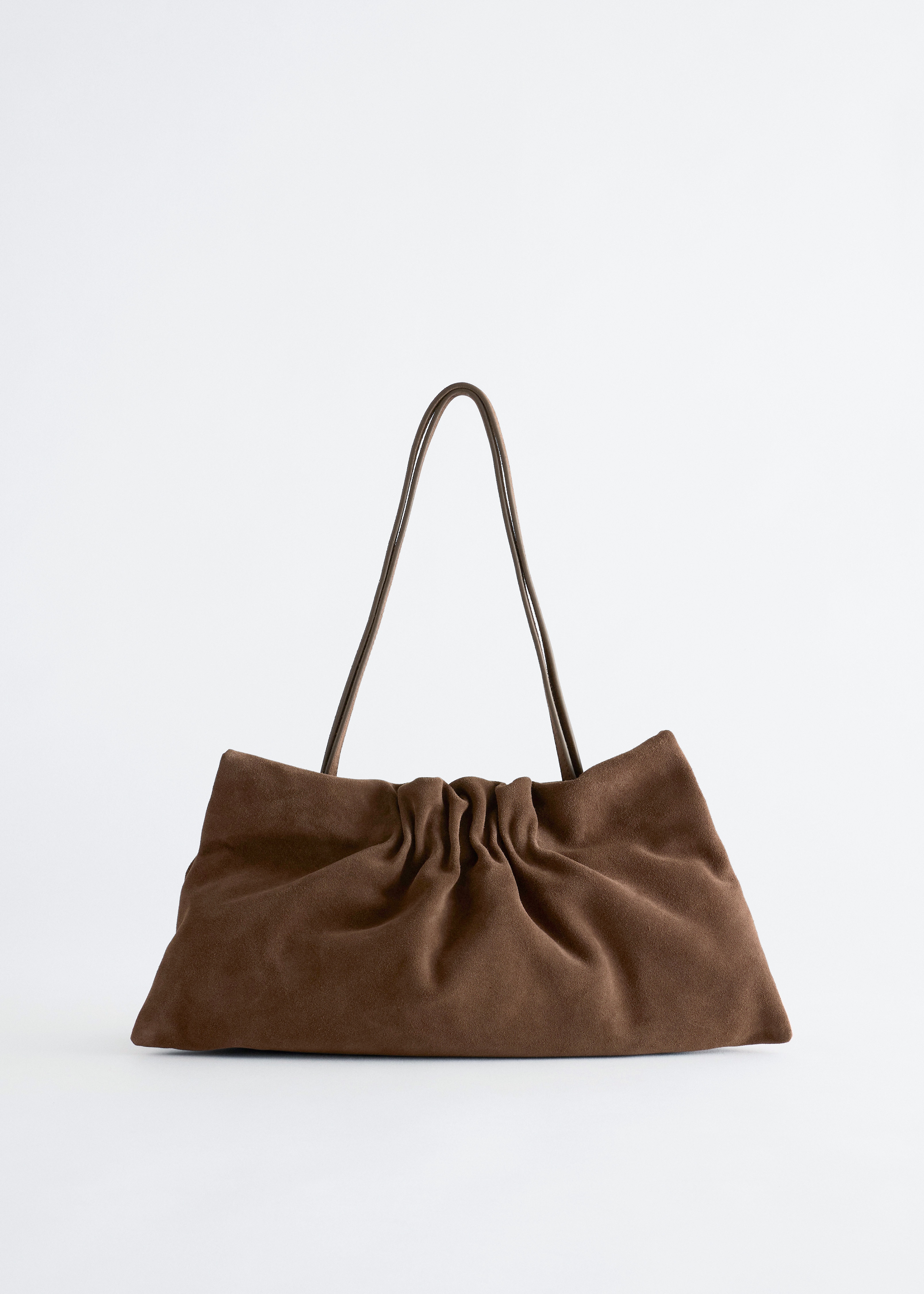 Una borsa a spalla marrone con effetto arricciato Ã¨ portata dalla modella, che la tiene con una mano contro un cappotto nero con cintura. La borsa presenta una struttura morbida e raccolta, con sottili spallacci in pelle drappeggiati sulla mano.