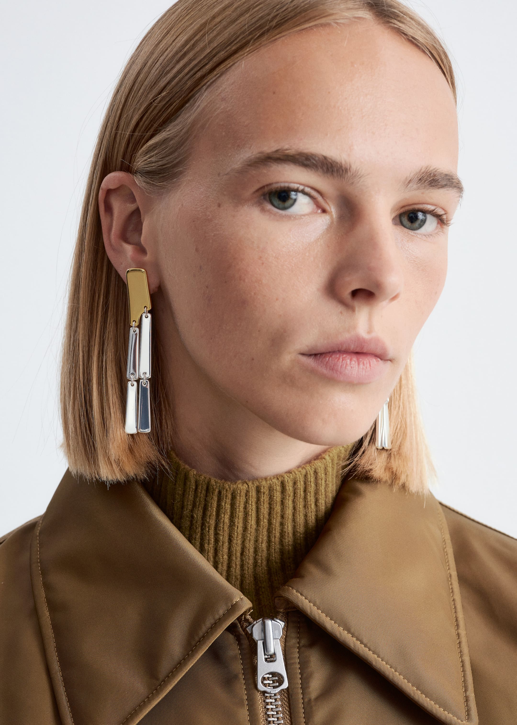 View larger image: A two-tone dangle earring is being worn on an ear, presenting its design from a slight forward angle. It features a rectangular gold-toned bar at the top, from which two smaller, rectangular silver-toned bars are hanging sequentially.