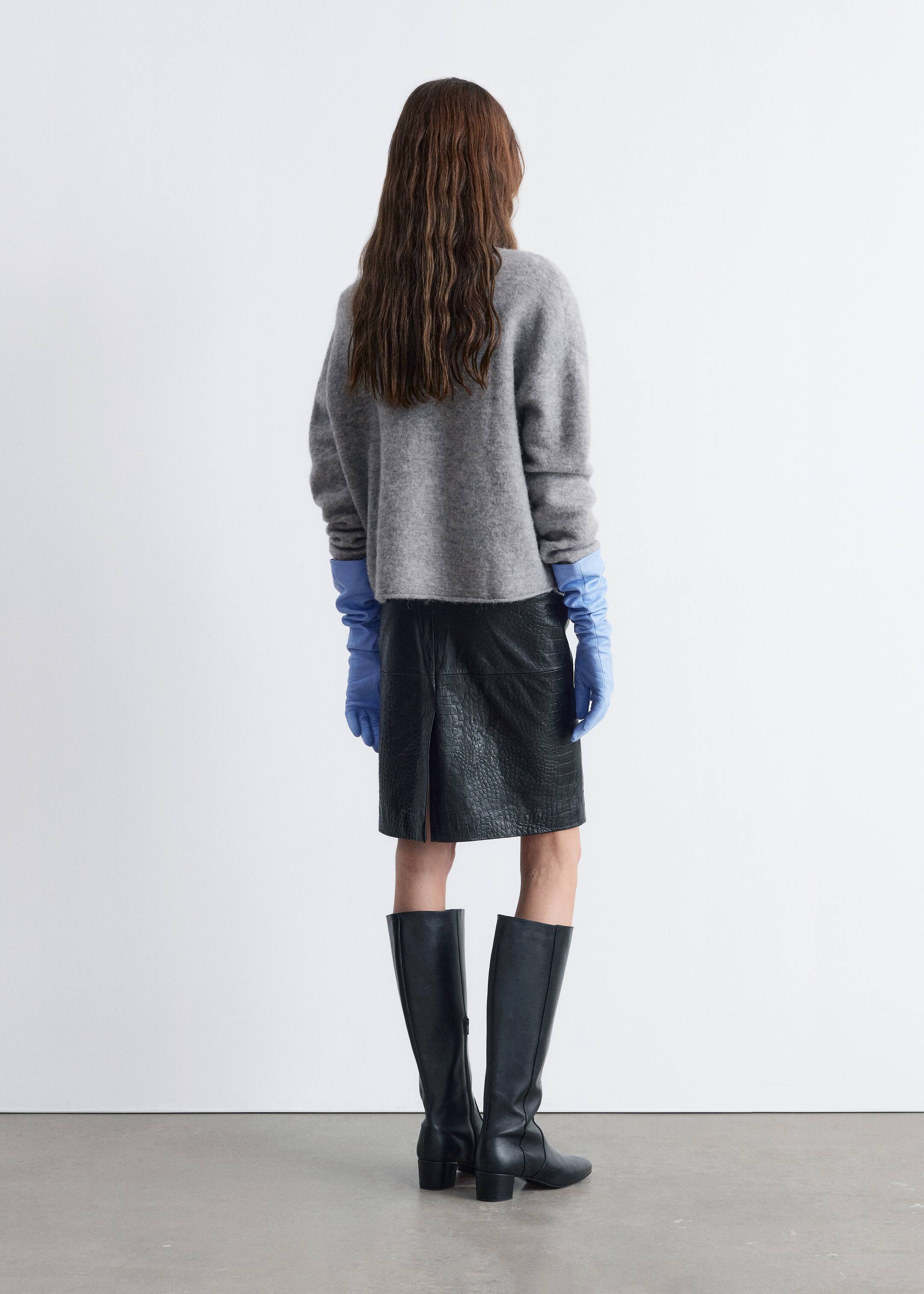 Se større billede: En grå, fuzzy sweater vises fra bagsiden, med en afslappet pasform og lange ærmer. Den er parret med en sort knælængde nederdel, der har en krokodilletekstur og en slids bagpå. Lange lyseblå handsker strækker sig ud fra under sweaterens ærmer, og sorte knæhøje støvler med blokhæle er synlige.