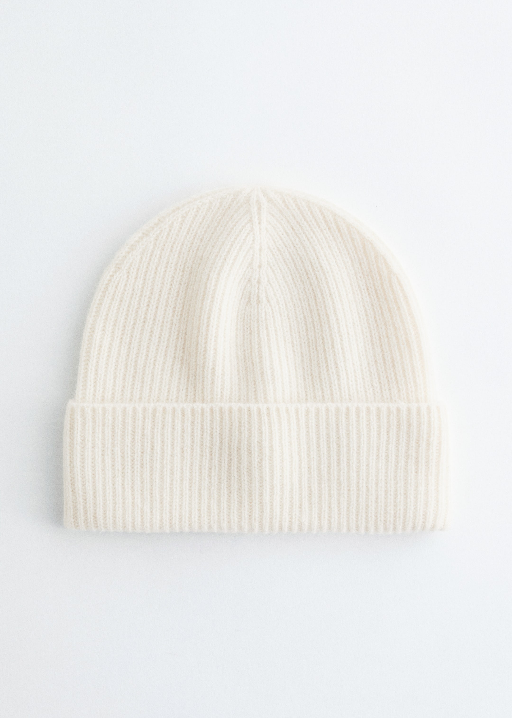 Größeres Bild anzeigen: Eine cremefarbene Mütze wird mit der Vorderseite präsentiert. Ihr Design zeigt ein gleichmäßiges Rippstrickmuster, und ein breiter Umschlagbund vervollständigt den unteren Rand.