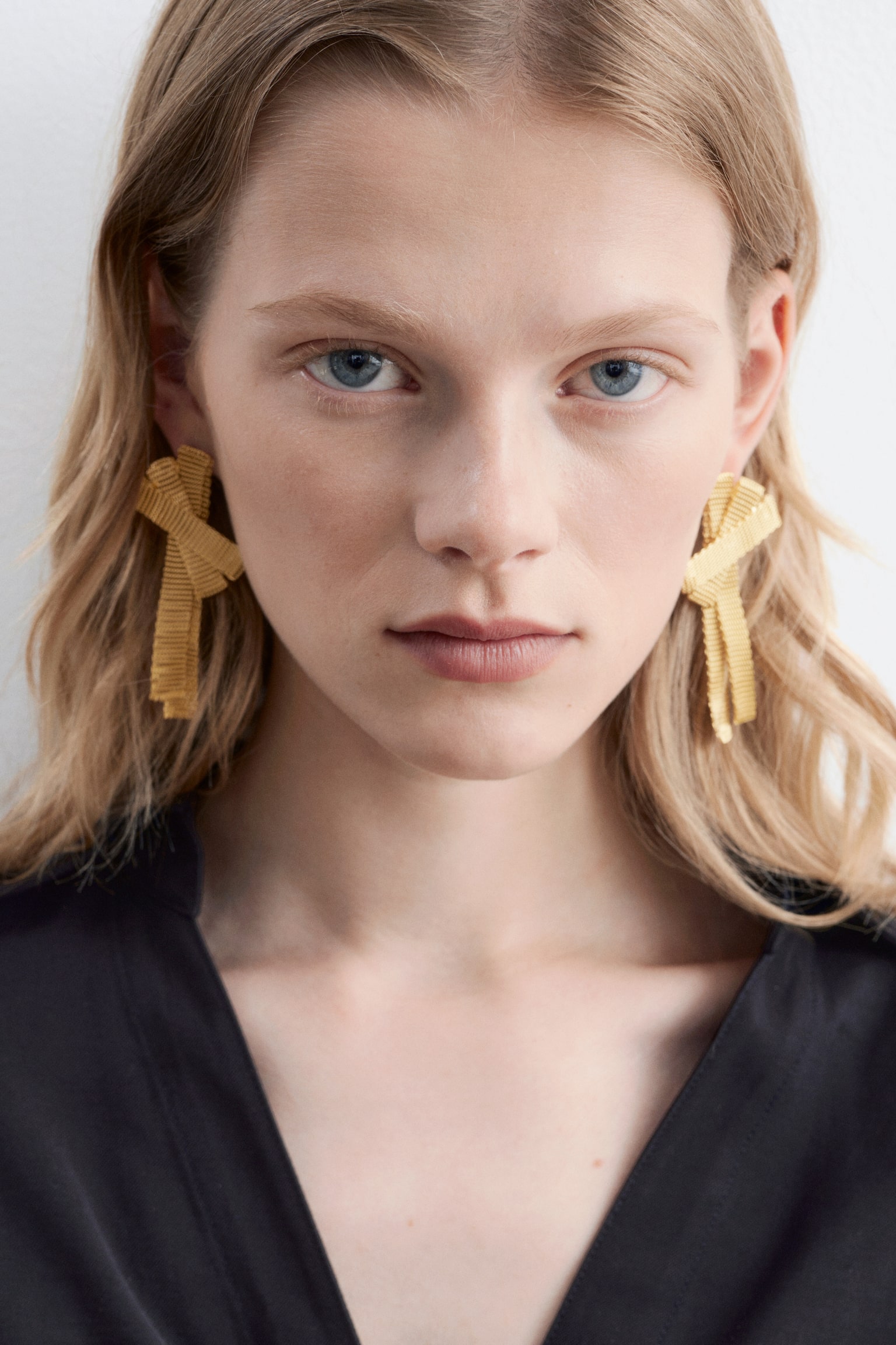 Boucles d'oreilles dorées arborant un design sculptural et texturé en forme de nœud. Chaque boucle d'oreille présente plusieurs bandes superposées et striées, offrant une vue de face sur chaque oreille. - 1