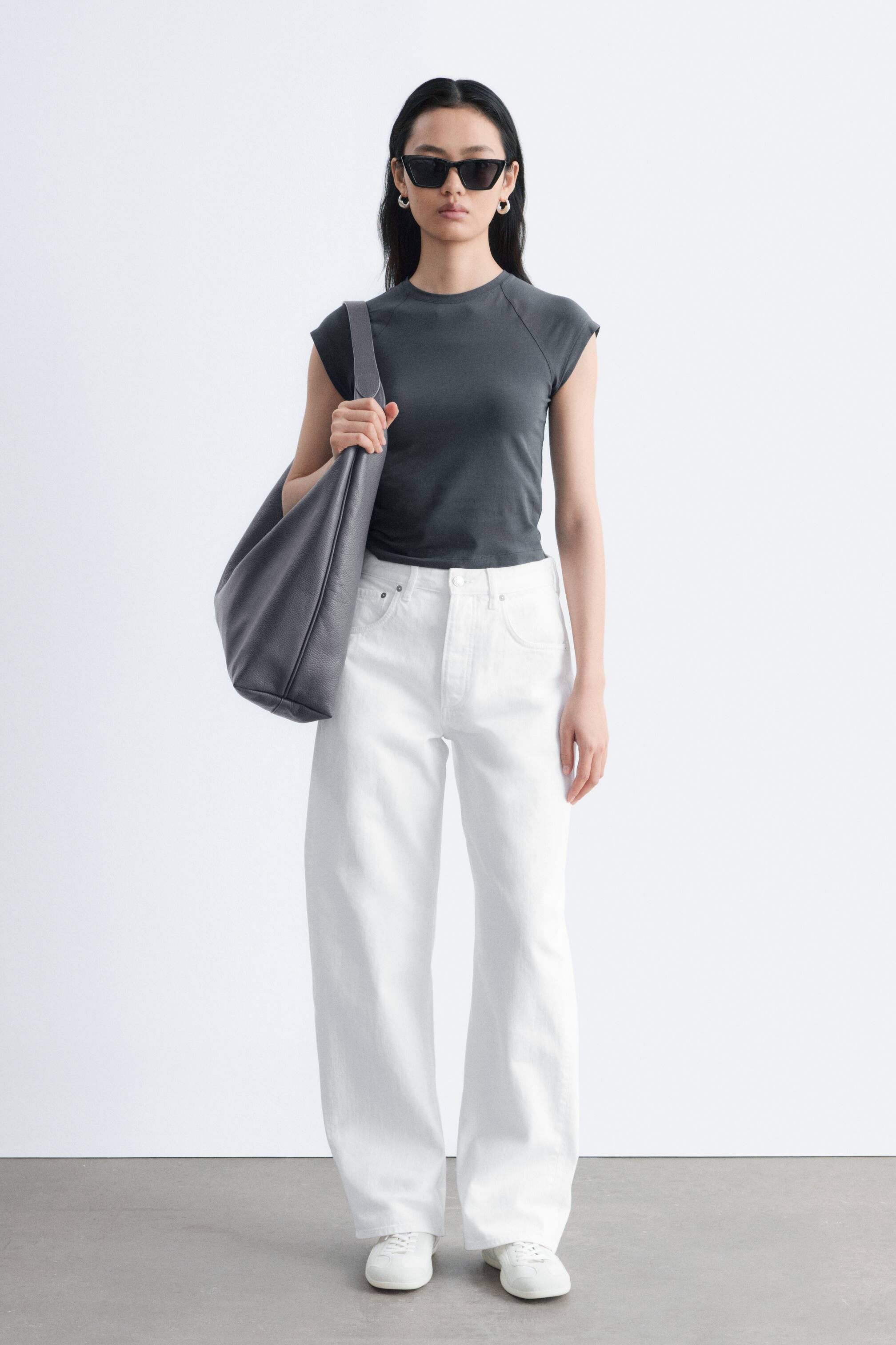 Se større billede: Hvide jeans har et højtaljet, bredt ben-snit med en afslappet pasform og går helt ned til gulvet, hvilket fremviser synlige forlommer med nitter.