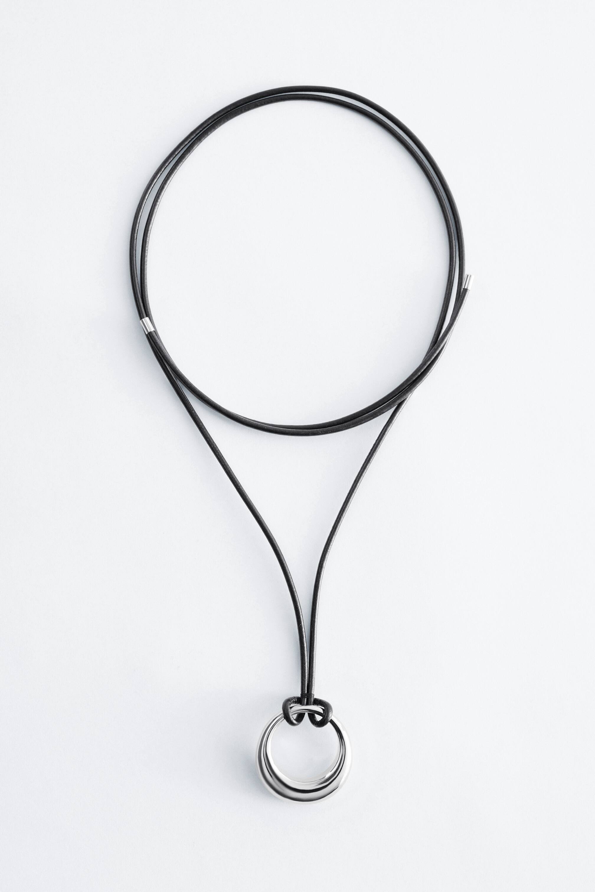 Visualizza immagine più grande: Collana con Ciondolo ad Anello in Pelle presenta un cordoncino in pelle nera, che forma un ampio anello nella parte superiore e si divide in due fili che fissano un ciondolo ad anello spesso, arrotondato e lucido con tonalità argento.