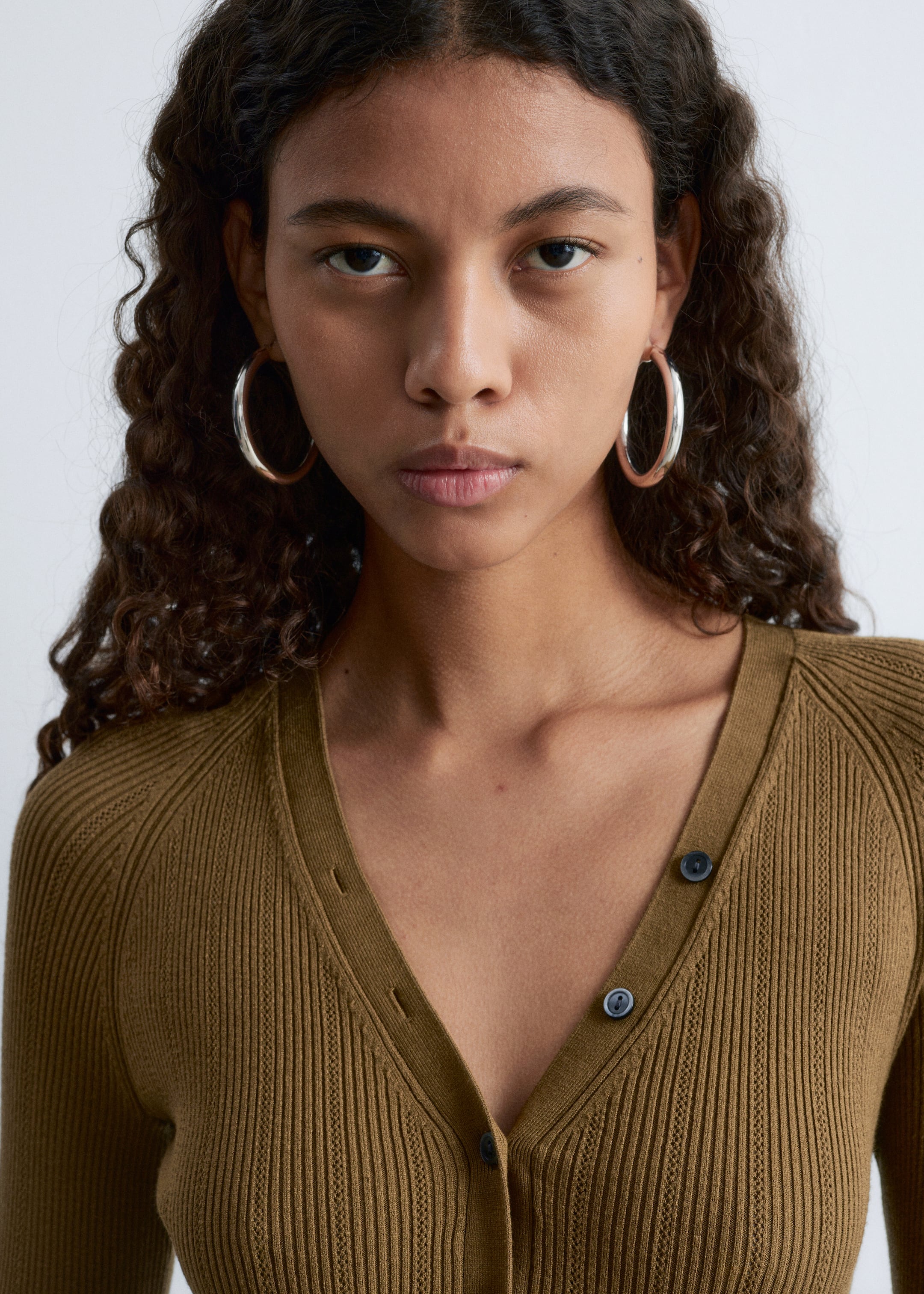 View larger image: An olive green ribbed knit cardigan is featuring a V-neckline with a button-front closure, displaying dark round buttons. It is presenting raglan sleeves and a fitted upper body from a front angle.