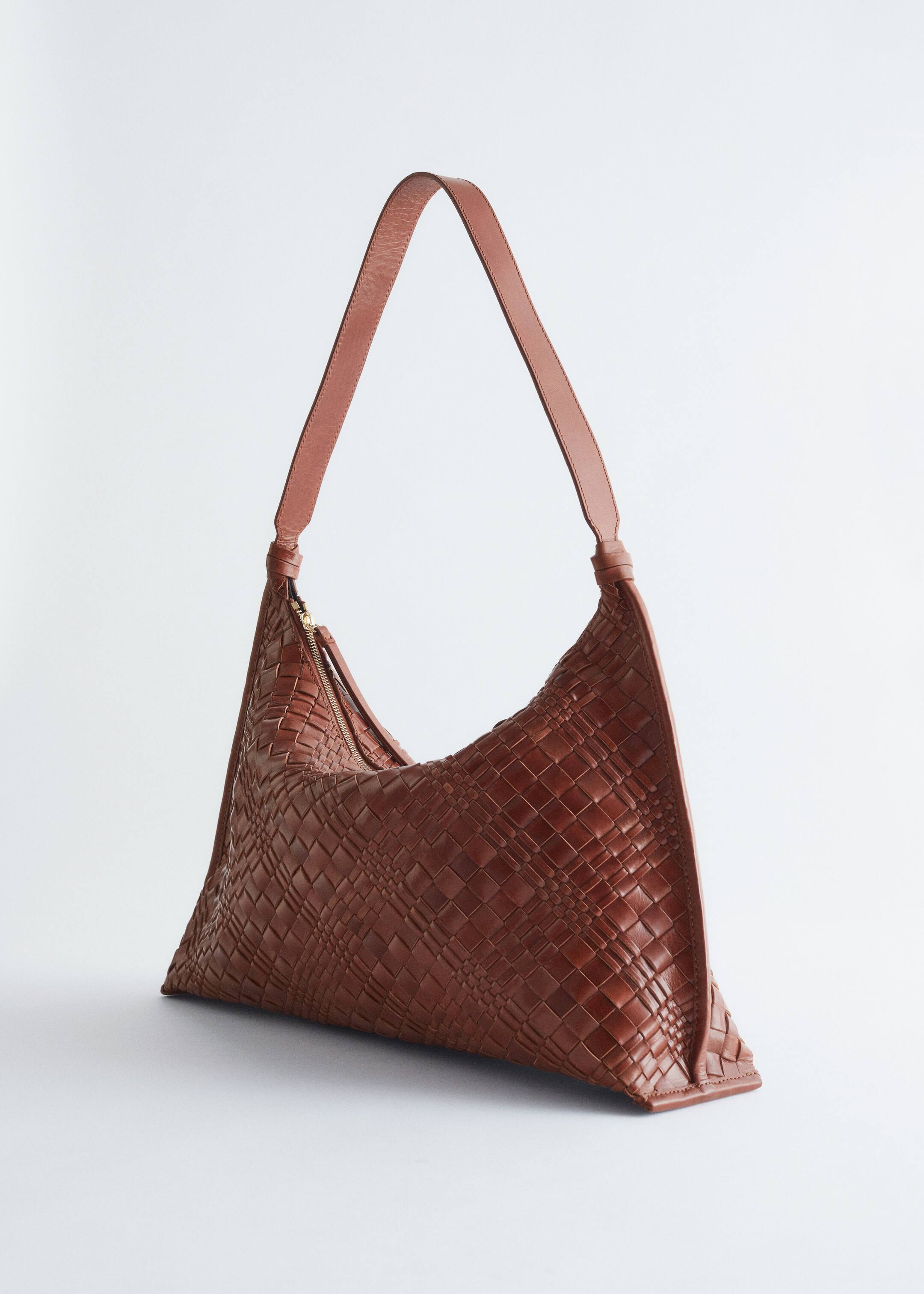 Größeres Bild anzeigen: Eine braune Ledertasche wird ausgestellt, die ein geflochtenes Design aus verflochtenen Lederbändern aufweist. Sie präsentiert einen gebogenen oberen Rand mit einem Reißverschluss und einem Lederzug sowie einen einzelnen Schulterriemen.