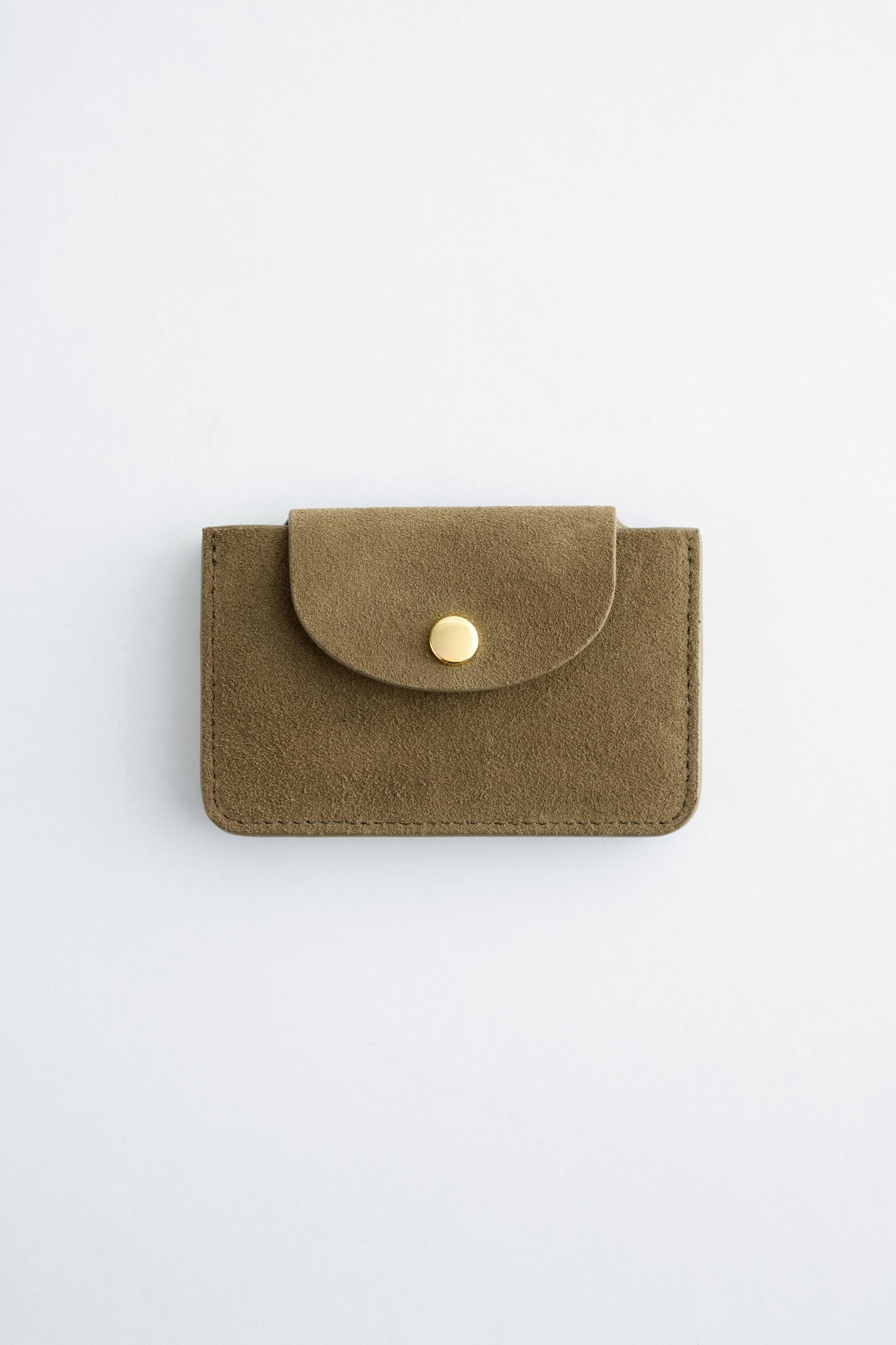 Vezi imaginea mai mare: Un suport pentru carduri este orientat frontal, realizat dintr-un material asemănător cu pielea întoarsă, de culoare verde măsliniu. Acesta prezintă un clapet rotunjit, securizat cu un singur închizător cu capse de culoare aurie, cu detalii de cusătură vizibile pe margini.