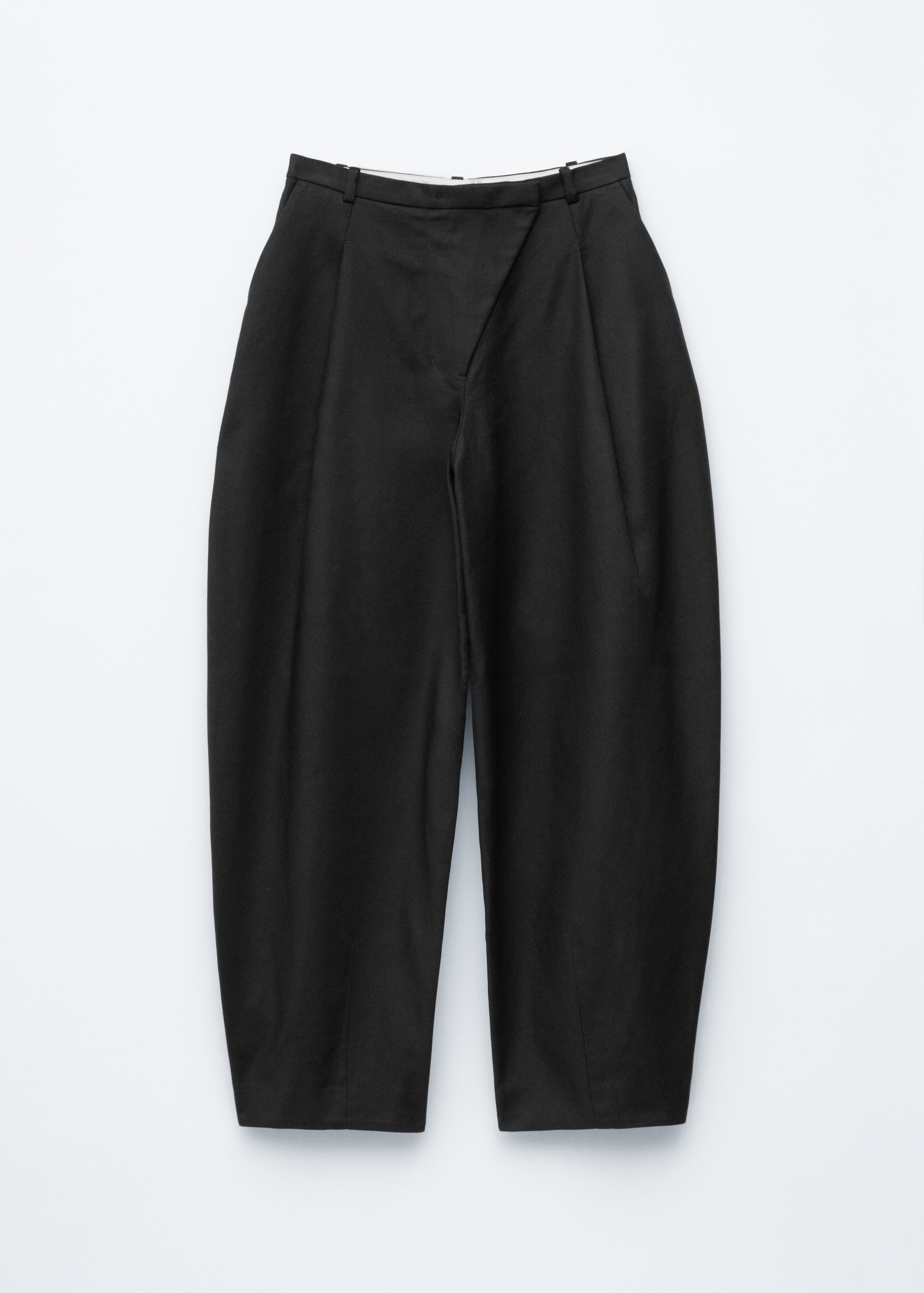 Agrandir l'image: Un pantalon noir présente une coupe ample avec des jambes en tonneau. L'avant présente une ceinture asymétrique et inclinée, avec une fermeture incorporant une braguette zippée et un crochet et barre, des plis verticaux visibles en dessous et des poches dans la couture latérale également présentes.