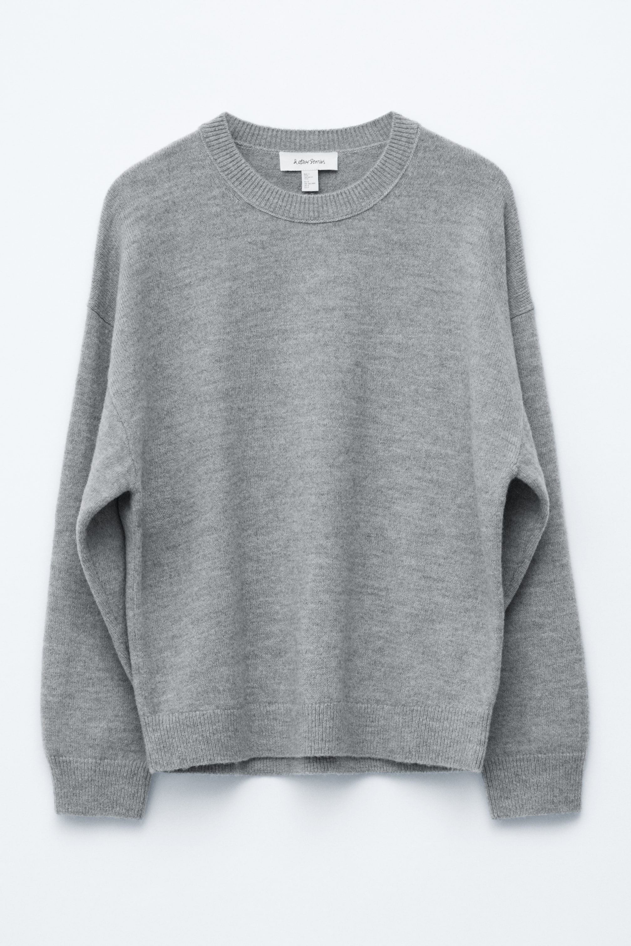 View larger image: A grey knitted jumper is being presented front-facing, featuring an oversized silhouette with dropped shoulders, long sleeves, a round ribbed neckline, and ribbed cuffs and hem. The jumper is displaying a soft, fuzzy knit texture.