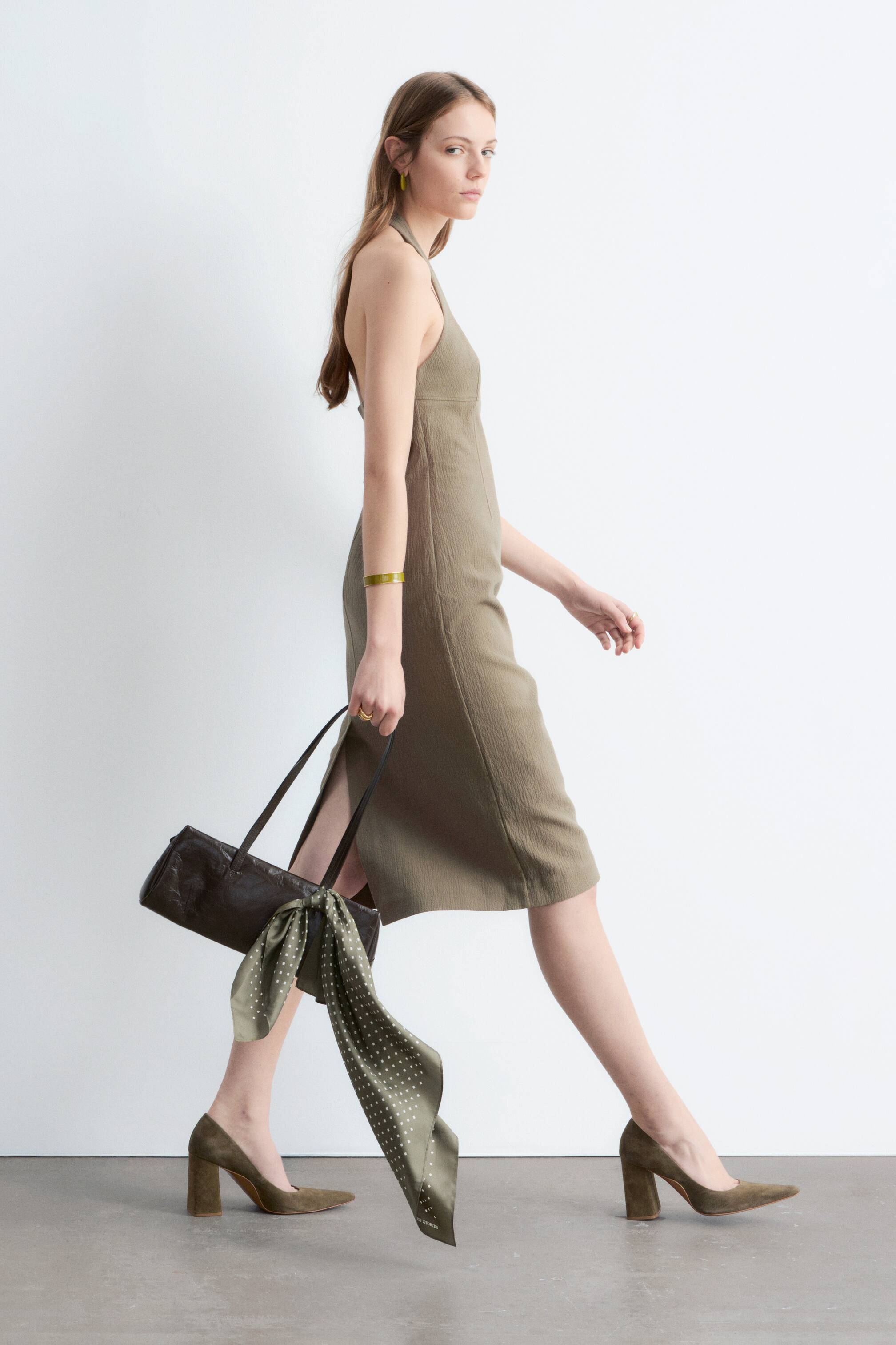 Agrandir l'image: Une robe midi dos-nu vert kaki en tissu texturé, avec une fente sur le côté gauche, présentée de profil afin de mettre en valeur sa silhouette complète.