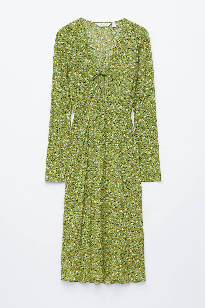 A FRONT view of a green midi dress showcases a small white and light green floral pattern. It features a V-neckline with a tie detail at the centre front and long sleeves. - 1