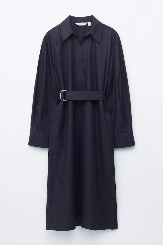 A dark midi dress is showcased FRONT, featuring a collar with a V-shaped opening and an adjustable belt cinching the waist with a silver-toned D-ring buckle. Long sleeves with buttoned cuffs extend from gently dropped shoulders, while side-seam pockets and slits at the hem complete the design. - 1