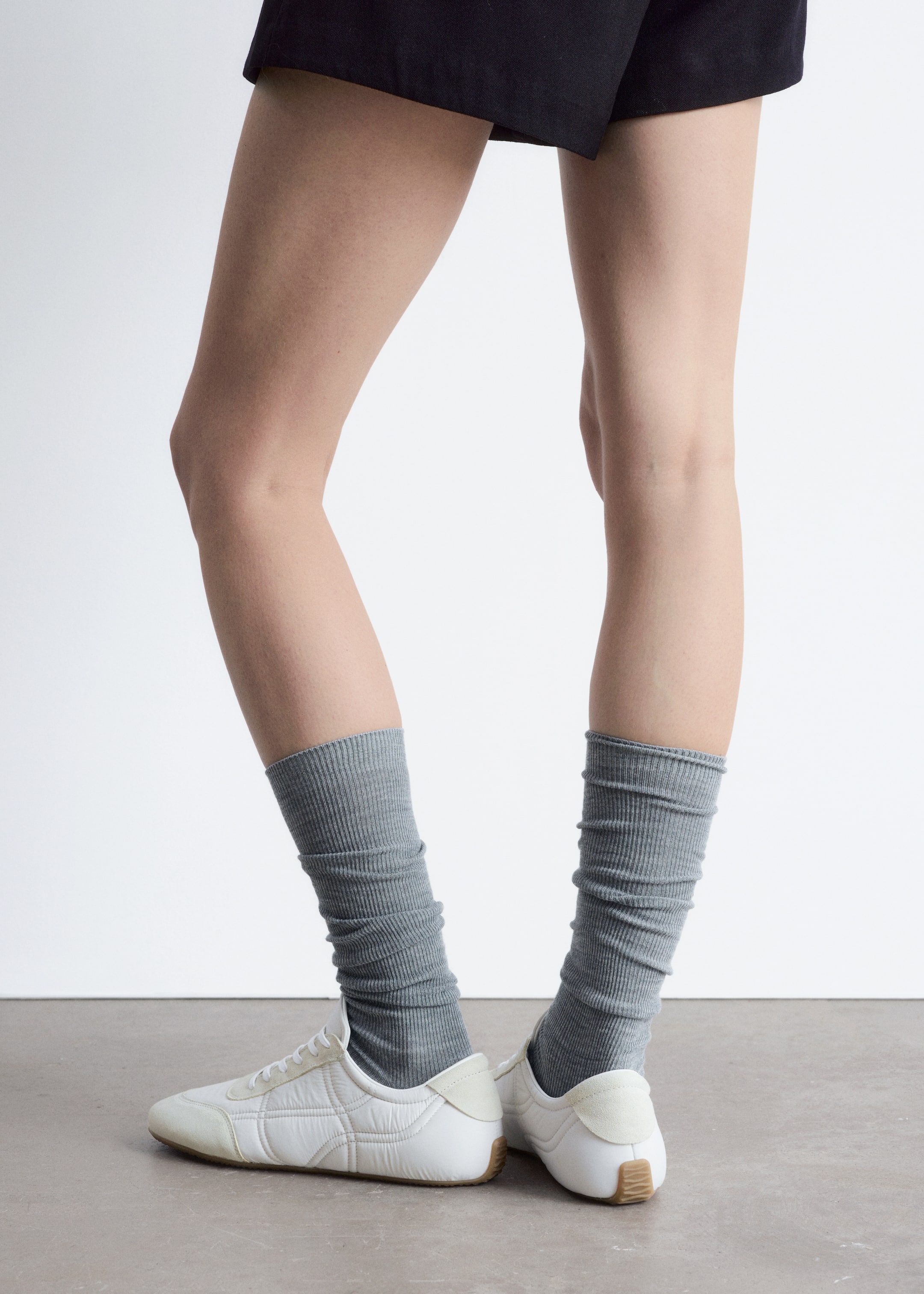 Agrandir l'image: Des chaussettes en tricot gris côtelé sont portées froncées sur les mollets et les chevilles, dépassant des baskets blanches.