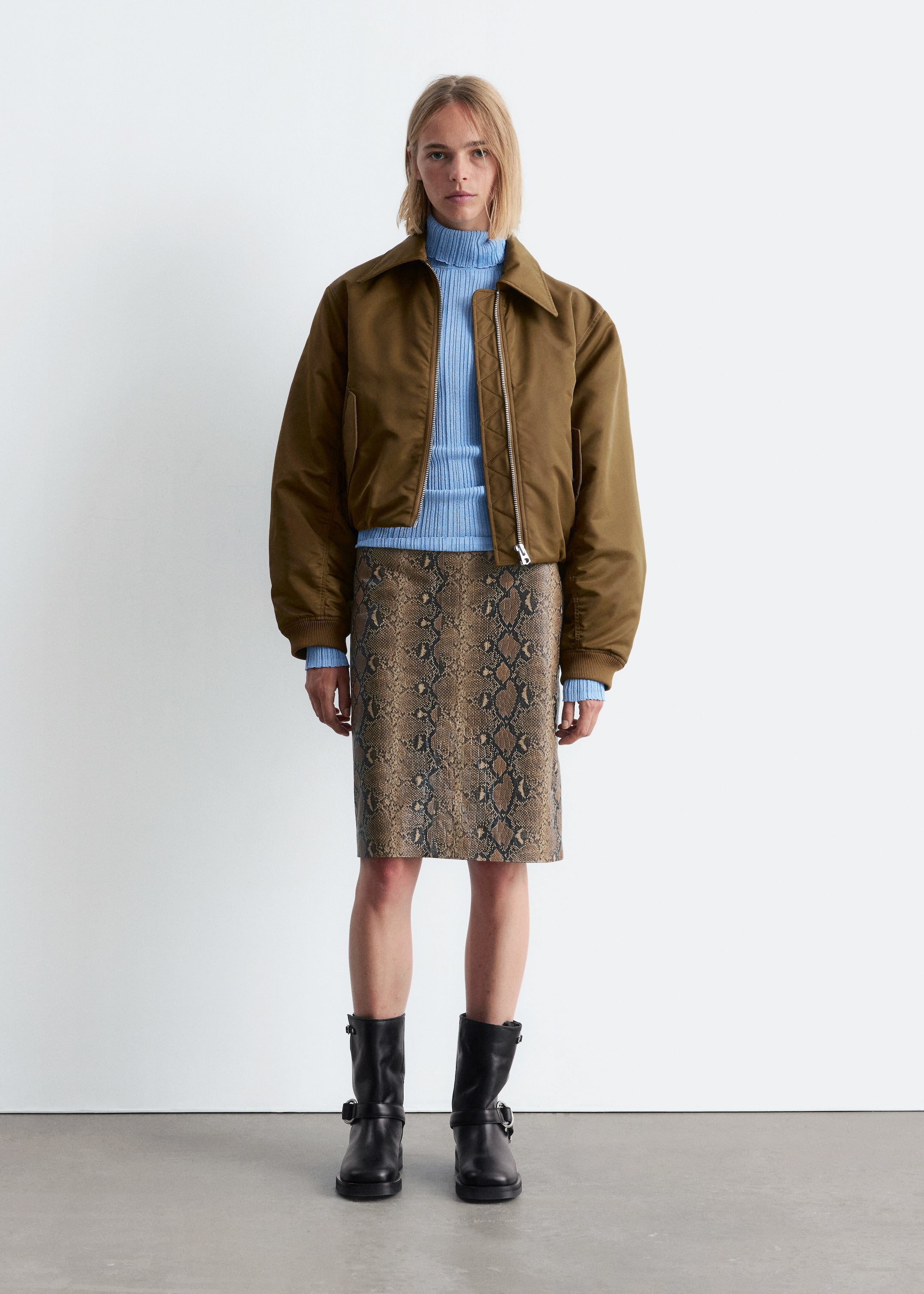 View larger image: A front-facing ensemble is being presented, featuring a brown cropped bomber jacket with a pointed collar and a prominent front zipper, layering over a light blue ribbed turtleneck sweater. A knee-length brown and black snakeskin print pencil skirt is being worn with black ankle boots featuring buckle straps.