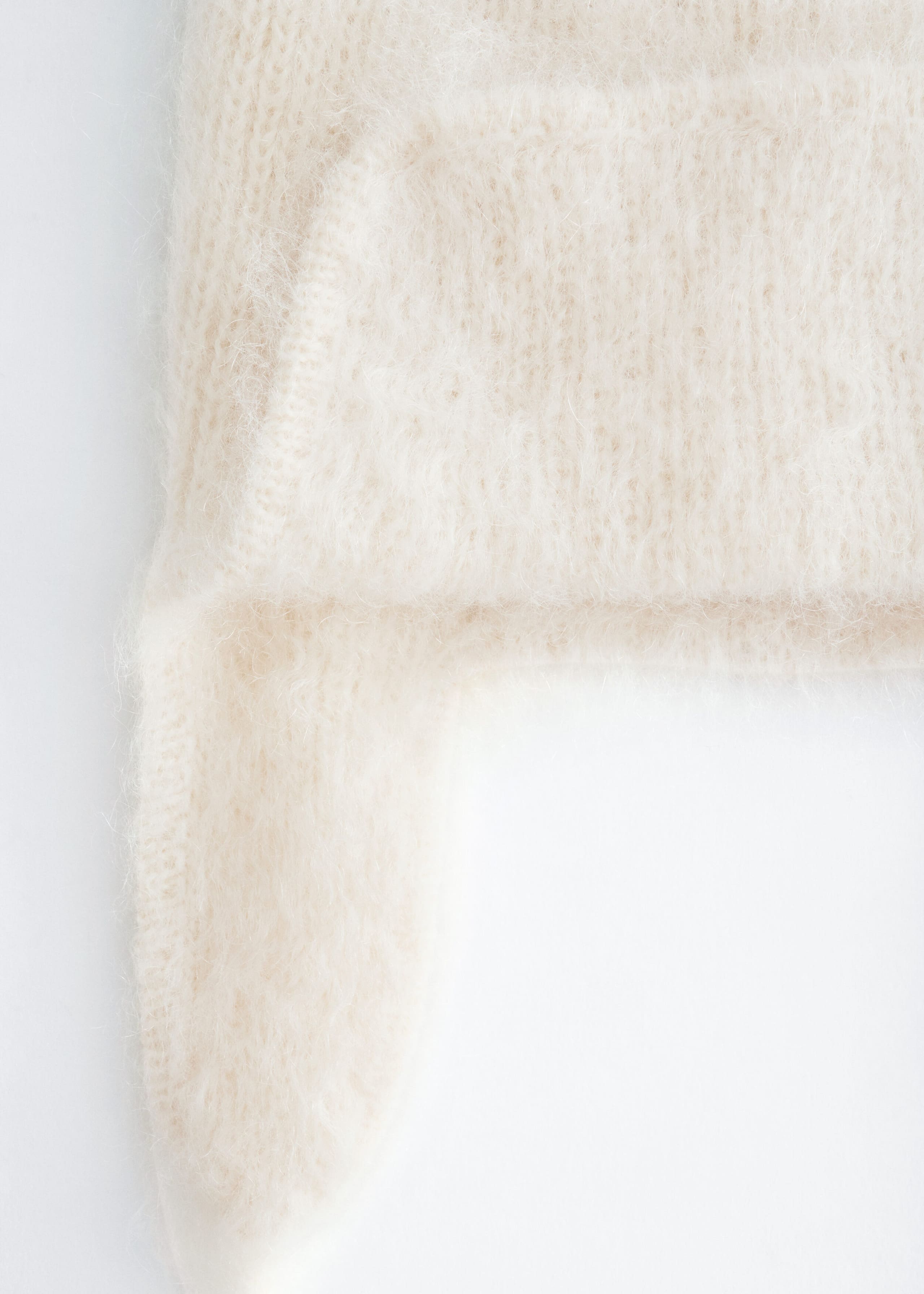A cream-colored knit trapper hat is shown in close-up, highlighting its soft, fuzzy brushed texture and the structured design of the ear flaps.