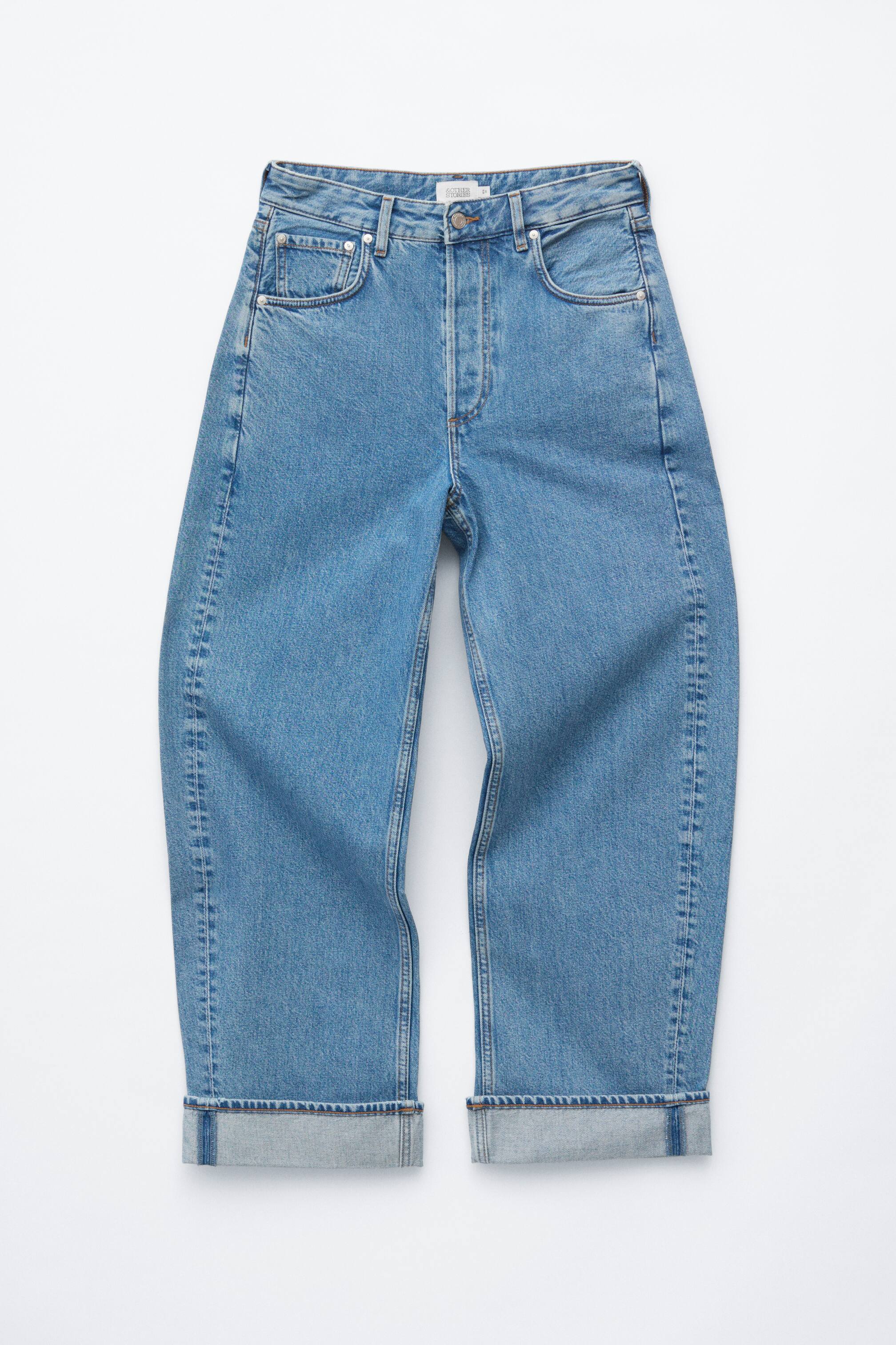 Agrandir l'image: Jean en denim bleu affichant un design classique à 5 poches à l'avant, avec une taille mi-haute, une braguette à boutons et des jambes surdimensionnées en forme de tonneau, actuellement stylisées avec des revers retroussés.