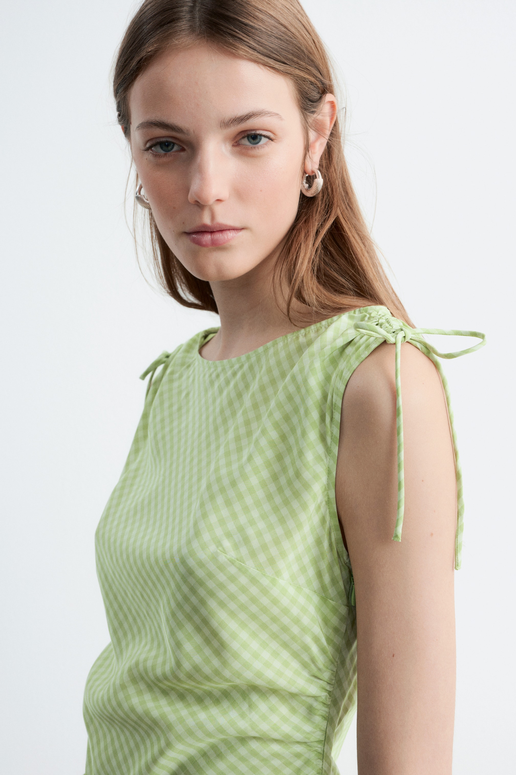 Vis større bilde: En grønn og hvit rutete ermeløs kjole med justerbare skulderbånd knyttet i sløyfer, bysteinnsnitt og rynker på siden. Modellen har på seg kjolen.