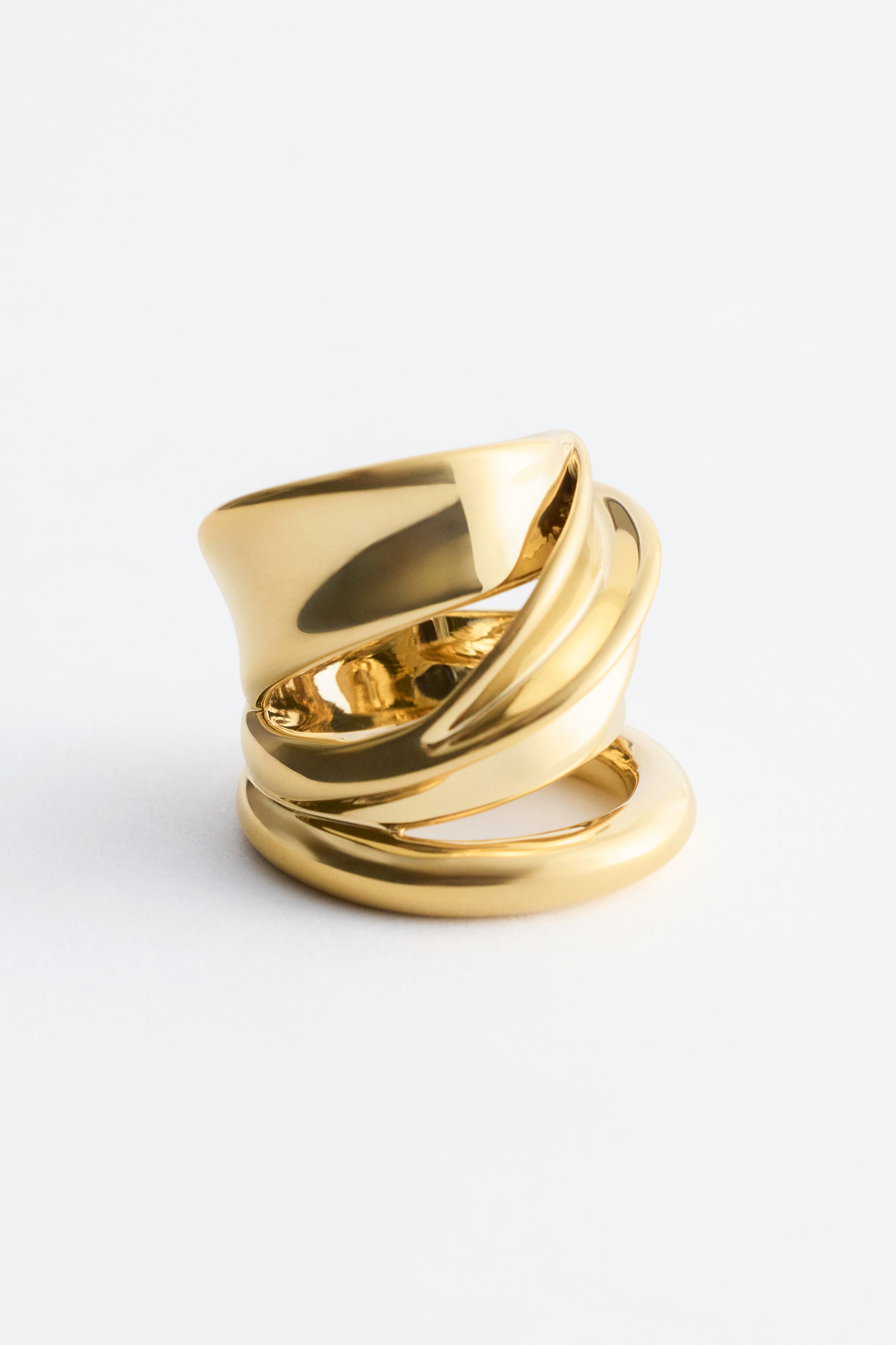 Größeres Bild ansehen: Ein klobiger, skulpturaler Ring aus poliertem Messing präsentiert sich mit einem doppelten Wickeldesign. Er wird in einem leichten Winkel gezeigt, um seine glatten, geschwungenen Bänder zu betonen.