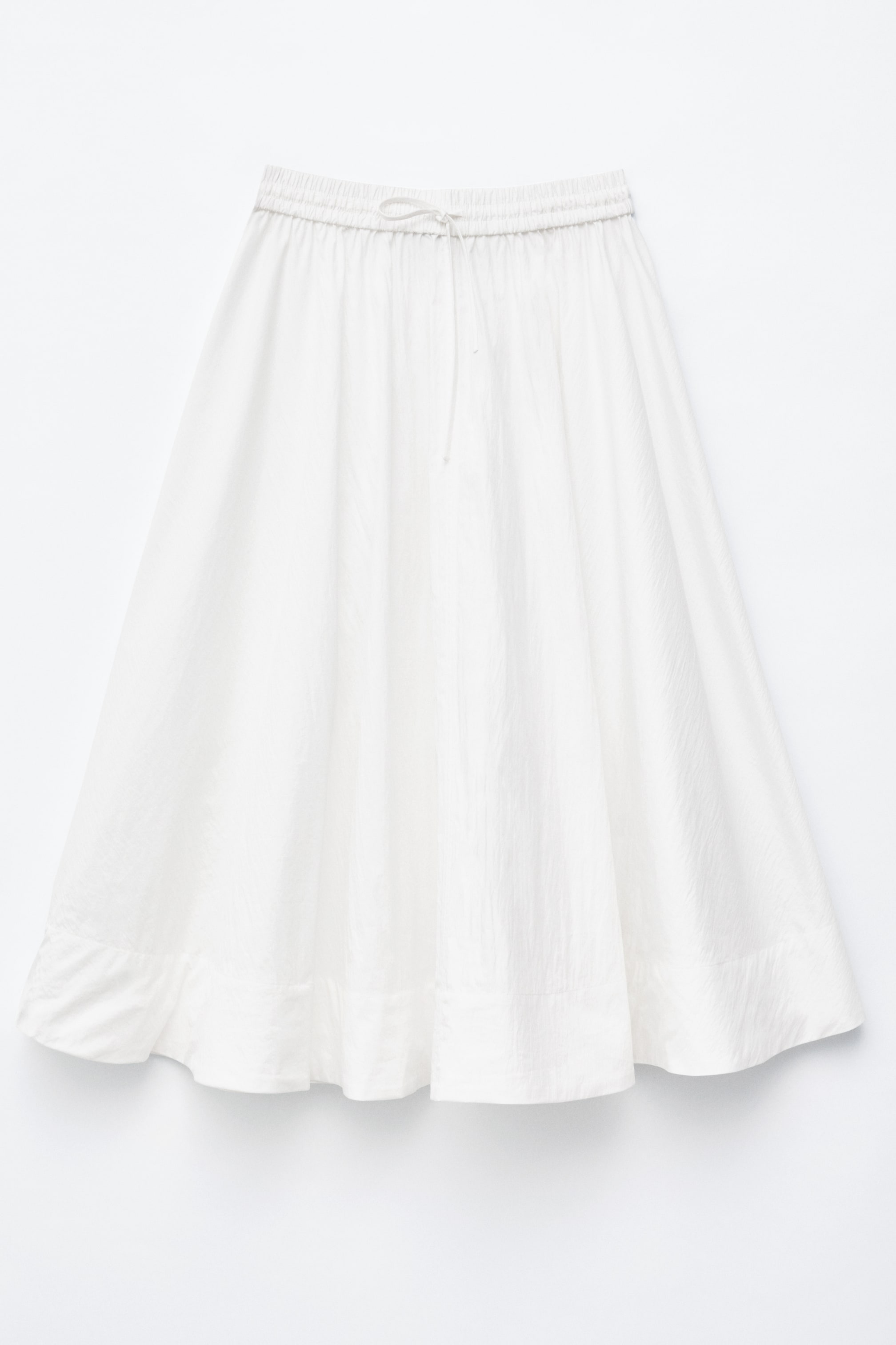 Ver imagem maior: Uma saia maxi branca está voltada para a frente, exibindo um cós elástico com um cordão ajustável. A saia reúne-se na cintura, criando uma forma volumosa em linha A.