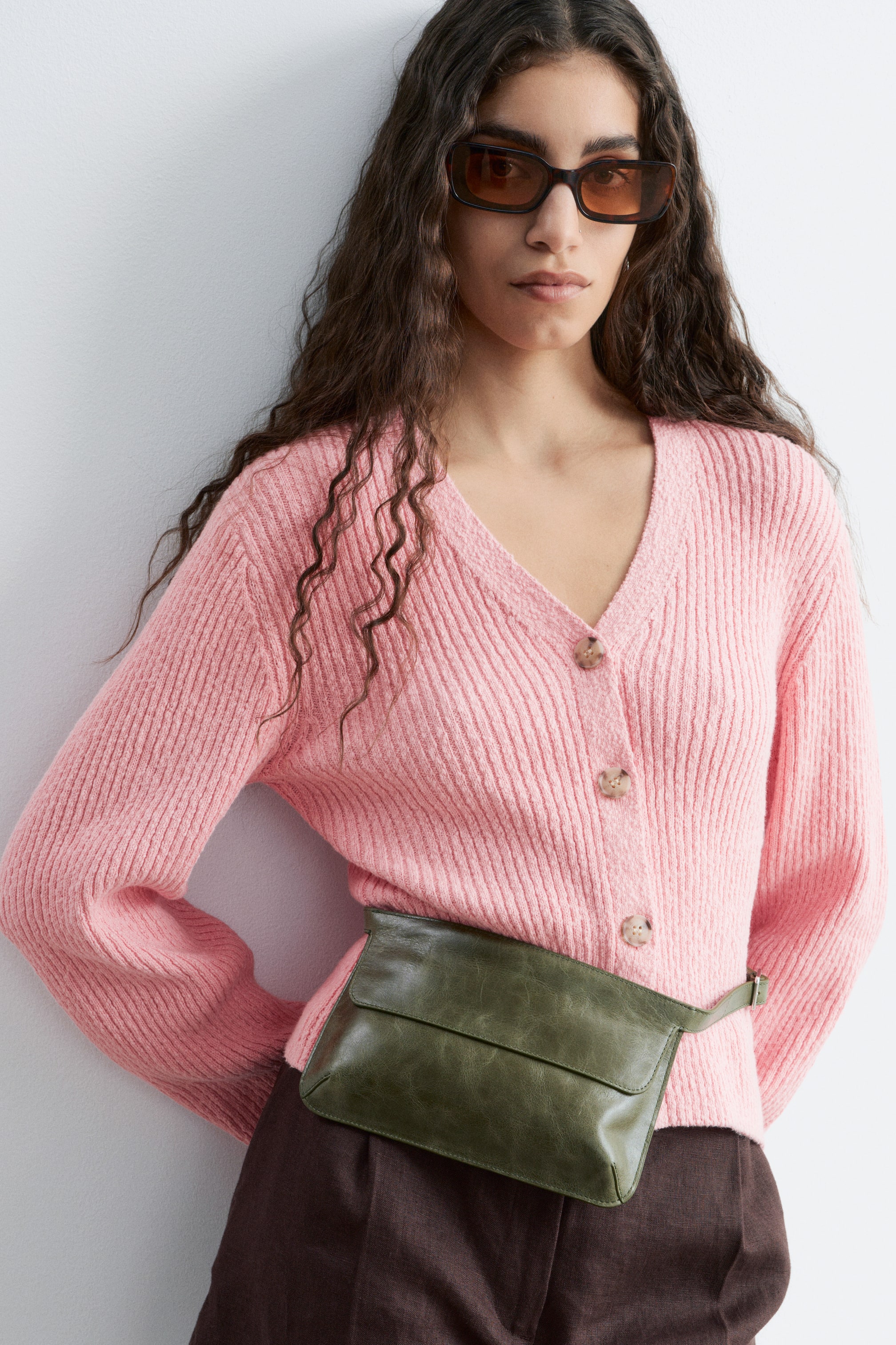 Visualizza l'immagine ingrandita: Cardigan rosa a maglia a coste con scollo a V e chiusura frontale con bottoni marrone chiaro. Presenta maniche lunghe e una borsa a cintura verde indossata sul davanti.