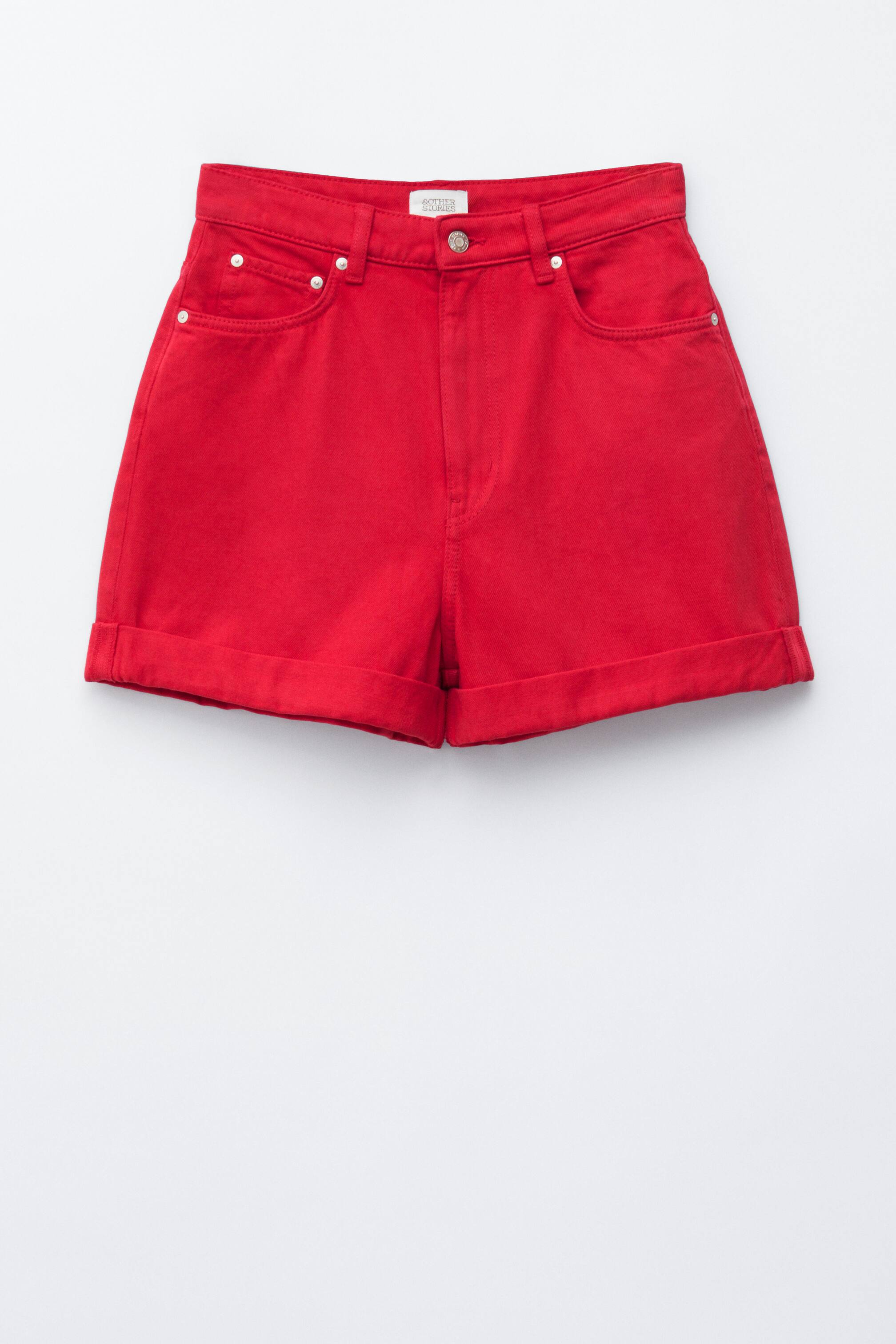 Ver imagem maior: Calções vermelhos de cintura alta apresentam um fecho frontal com um botão prateado e uma pequena etiqueta da marca na cintura. Incluem passadeiras para cinto, dois bolsos frontais com rebites prateados e bainhas dobradas.