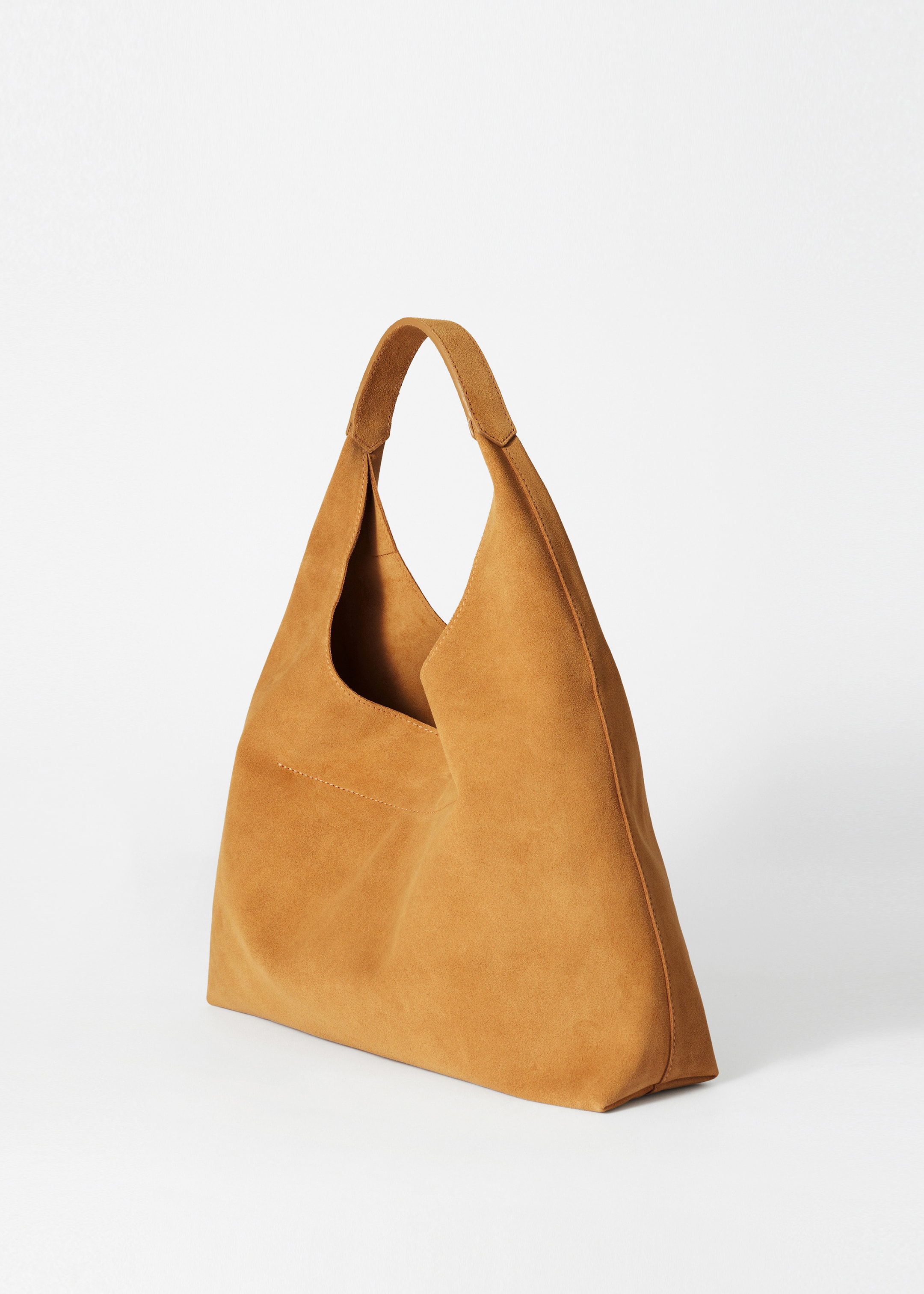View larger image: A slouchy tan suede tote bag is standing, angled to the right. It is showcasing its smooth, matte finish, a single wide handle attached at the top corners, and a subtle horizontal stitch line on its front panel.