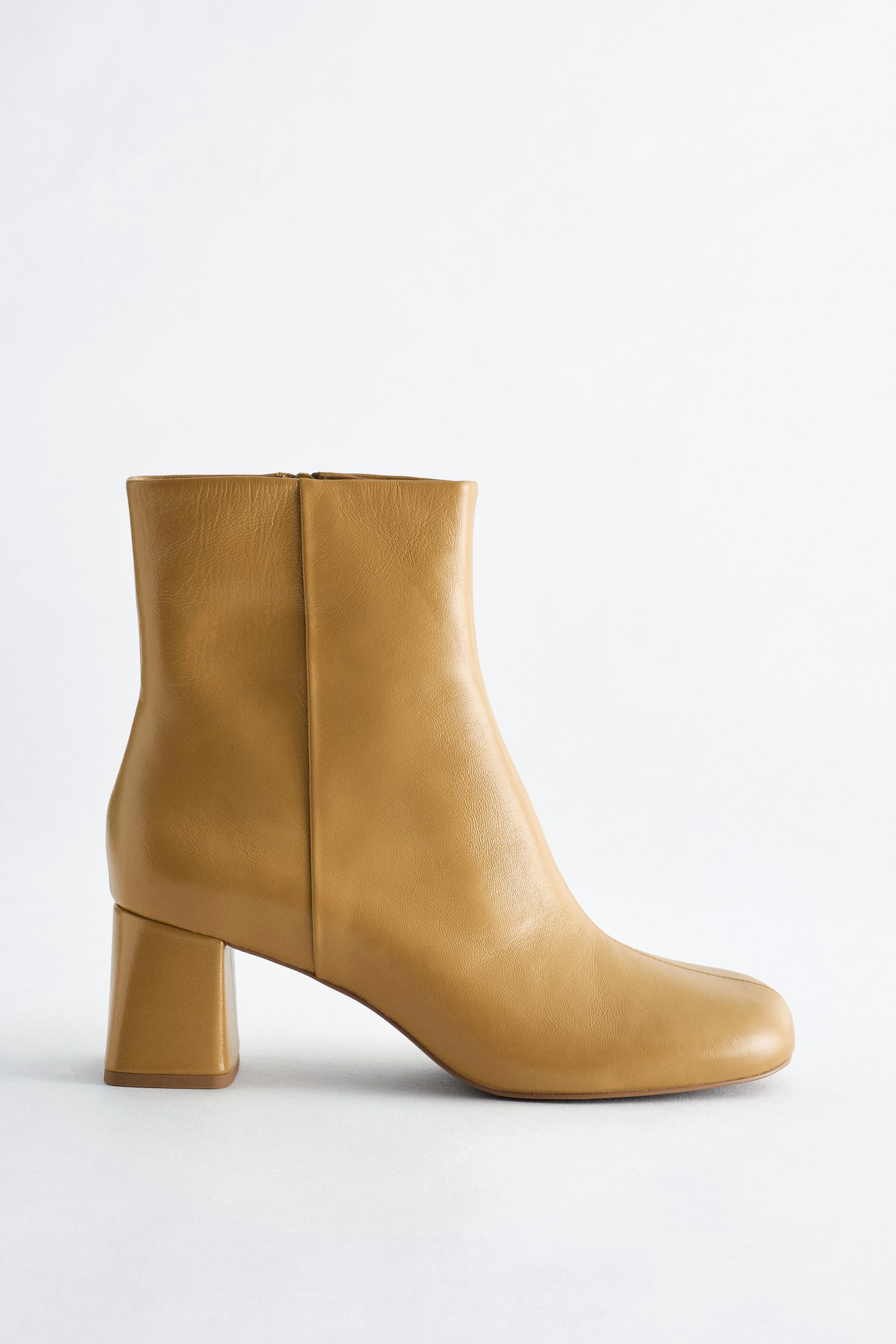 Une botte chelsea en cuir couleur ocre est prÃ©sentÃ©e de profil, avec un bout arrondi et une tige ajustÃ©e Ã  la cheville. La botte est dotÃ©e dâun talon bloc assorti de hauteur moyenne et dâune couture verticale nette courant le long du cÃ´tÃ©.