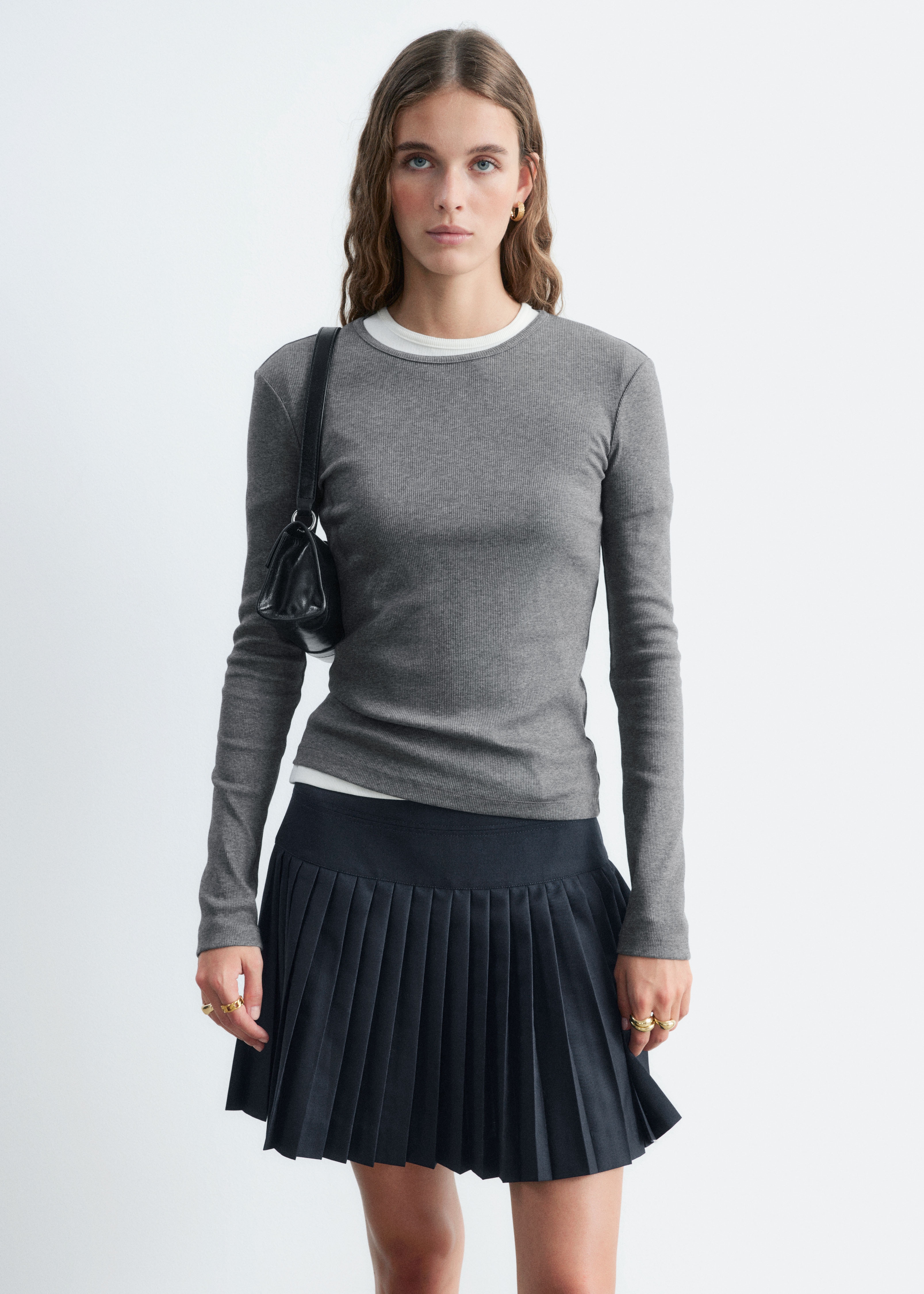 Ein graues Langarmshirt mit Rippstruktur ist mit einer feinen gerippten Stricktextur zu sehen, frontal dargestellt. Das Oberteil zeigt einen klassischen Rundhalsausschnitt, lange, eng anliegende Ãrmel und einen geraden Saum.