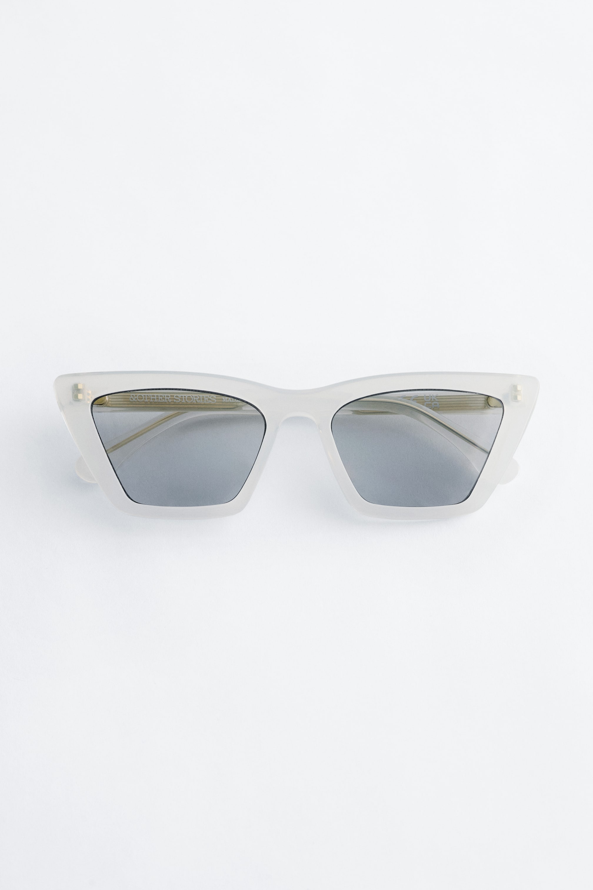 Größeres Bild ansehen: Anguläre Katzenaugen-Sonnenbrillen präsentieren sich mit einem durchscheinenden hellgrauen Rahmen, der scharfe, nach oben geschwungene äußere Ecken und leicht quadratische untere Kanten aufweist. Sie sind mit dunklen, reflektierenden Gläsern ausgestattet und werden frontal präsentiert.