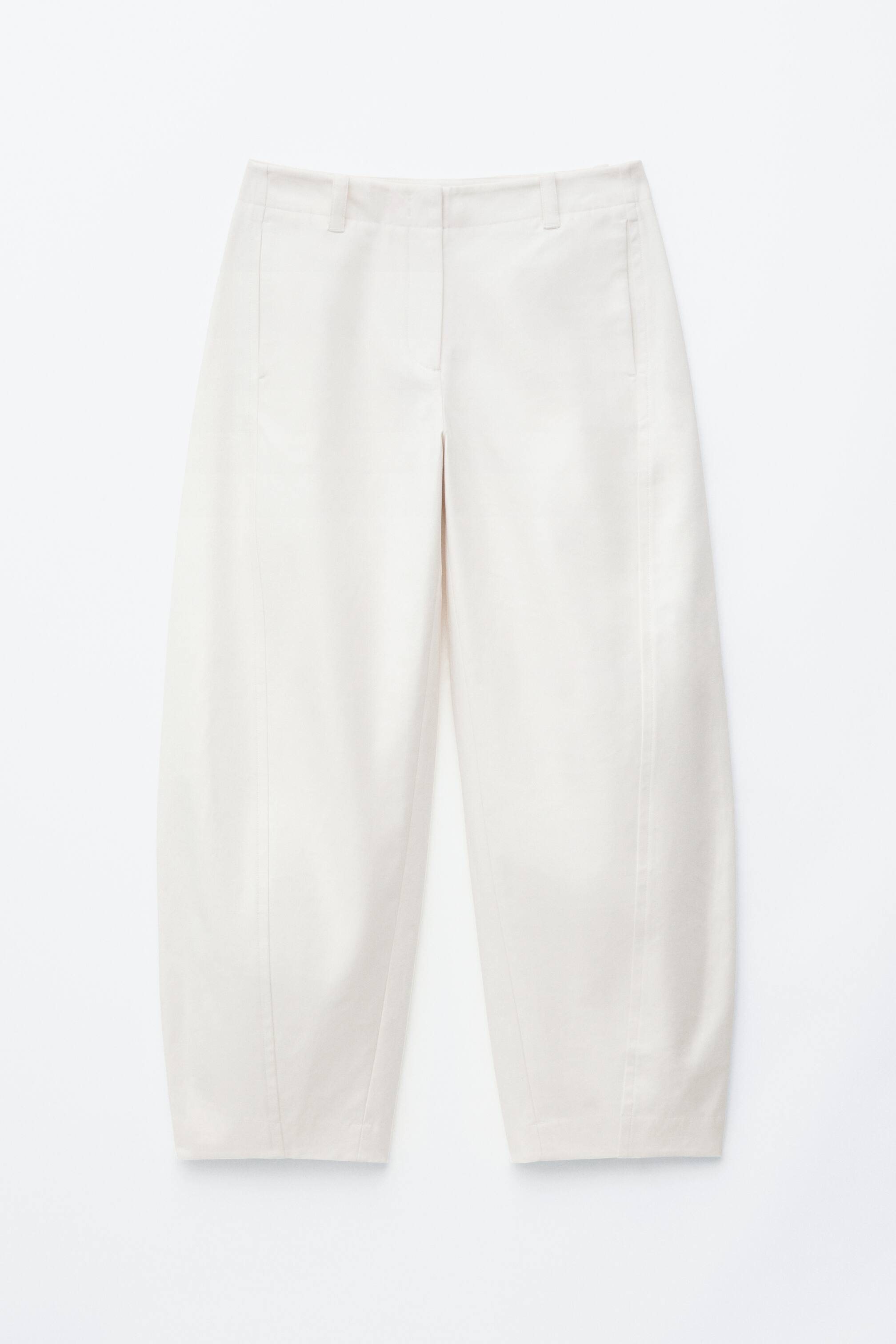 Προβολή μεγαλύτερης εικόνας: Τα παντελόνια σε κρεμ απόχρωση παρουσιάζονται από μπροστινή όψη, διαθέτοντας επίπεδη ζώνη μέσης με θηλιές για ζώνη, κρυφό μπροστινό κλείσιμο και λοξές πλαϊνές τσέπες. Κάθετο ράψιμο διατρέχει το μπροστινό μέρος κάθε ποδιού, διαμορφώνοντας μια φουσκωτή, κωνική σιλουέτα που καταλήγει στον αστράγαλο.