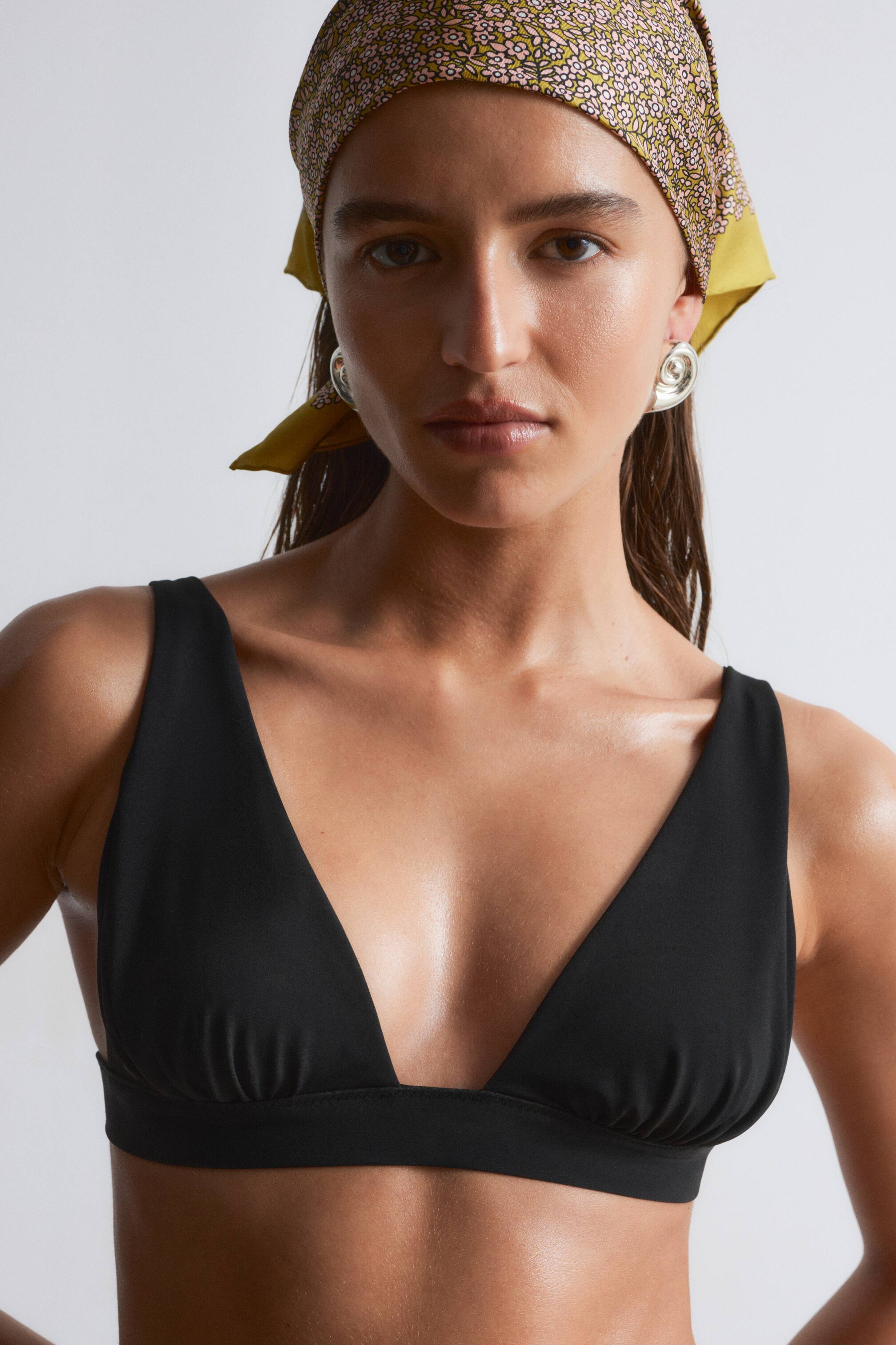 Visualizza l'immagine ingrandita: Un top bikini nero viene presentato, caratterizzato da una profonda scollatura a V e coppe triangolari. È progettato con spalline larghe e una fascia sottoseno ampia, mostrando una leggera arricciatura sotto le coppe.