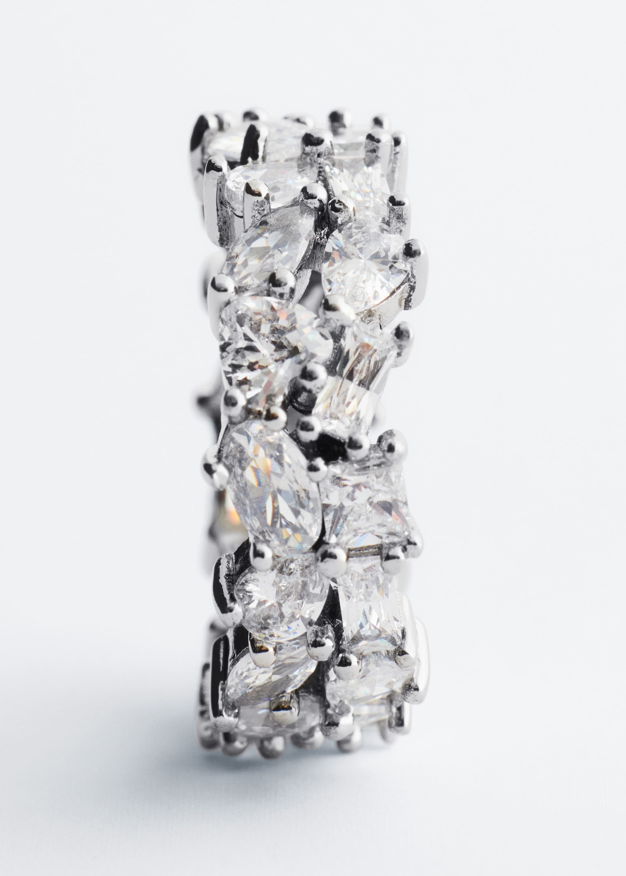 A wide silver-tone band ring is standing upright, showcasing a dense, sparkling cluster of mixed-cut cubic zirconia stones in prong settings.