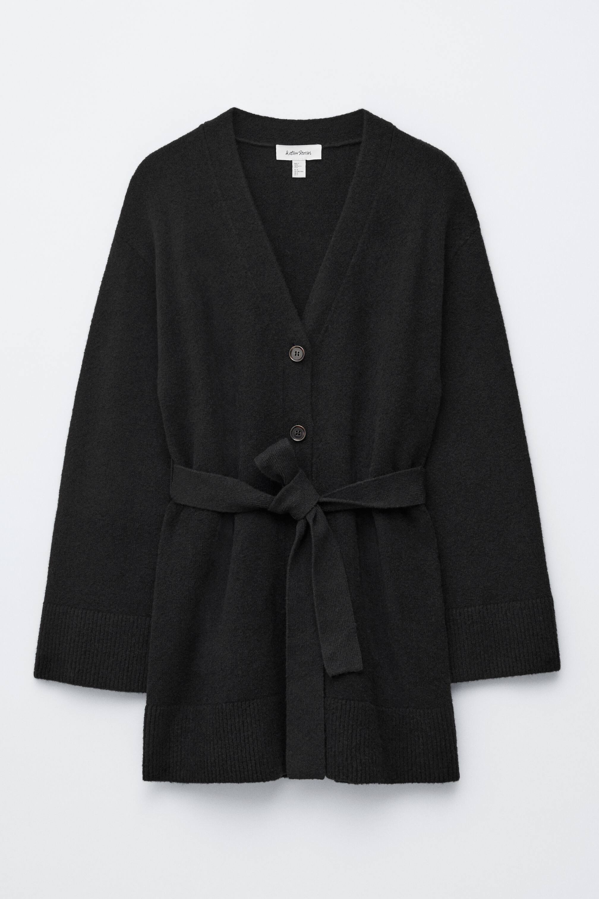 Agrandir l'image: Un cardigan noir est présenté de face, avec un col en V et deux boutons sombres sur le devant. Il est cintré à la taille par une ceinture en tissu assorti nouée en un nœud, et est complété par de longues manches larges avec des poignets côtelés et un ourlet côtelé.