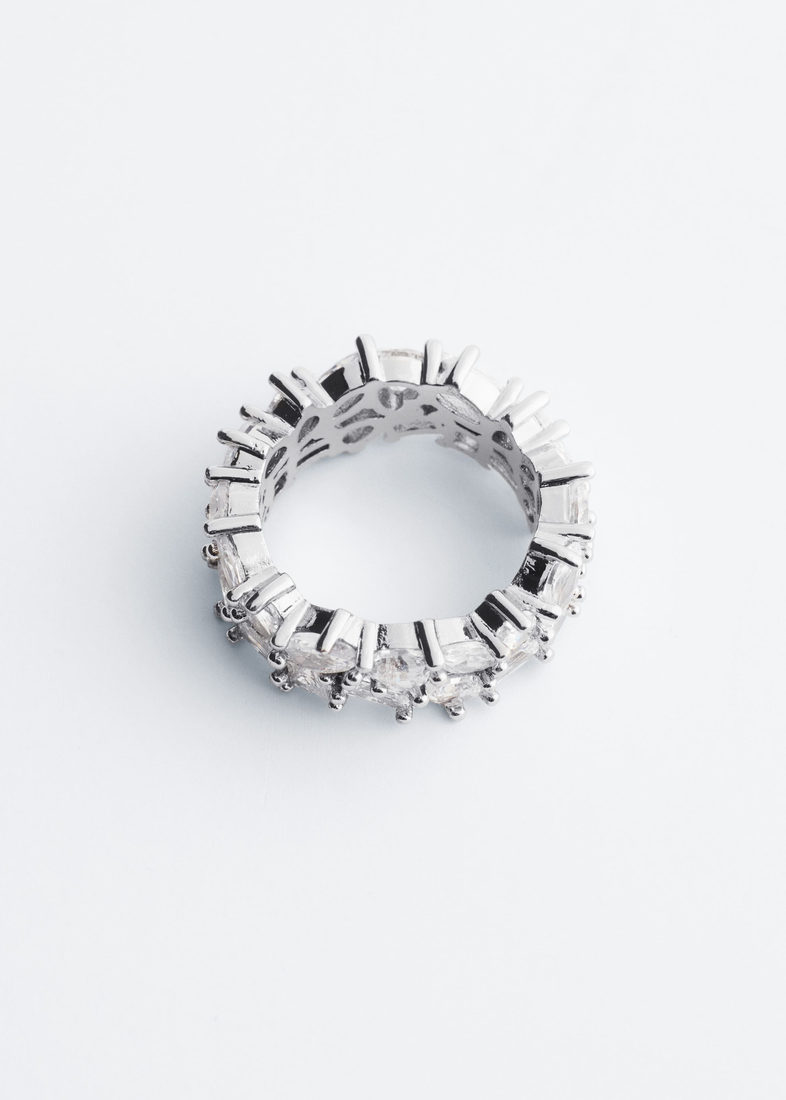 A silver-toned ring, shown from the top, featuring a wide band set with a clustered arrangement of mixed-cut cubic zirconia stones. The clear, faceted stones line the entire outer band and are secured by prominent silver-toned prongs.