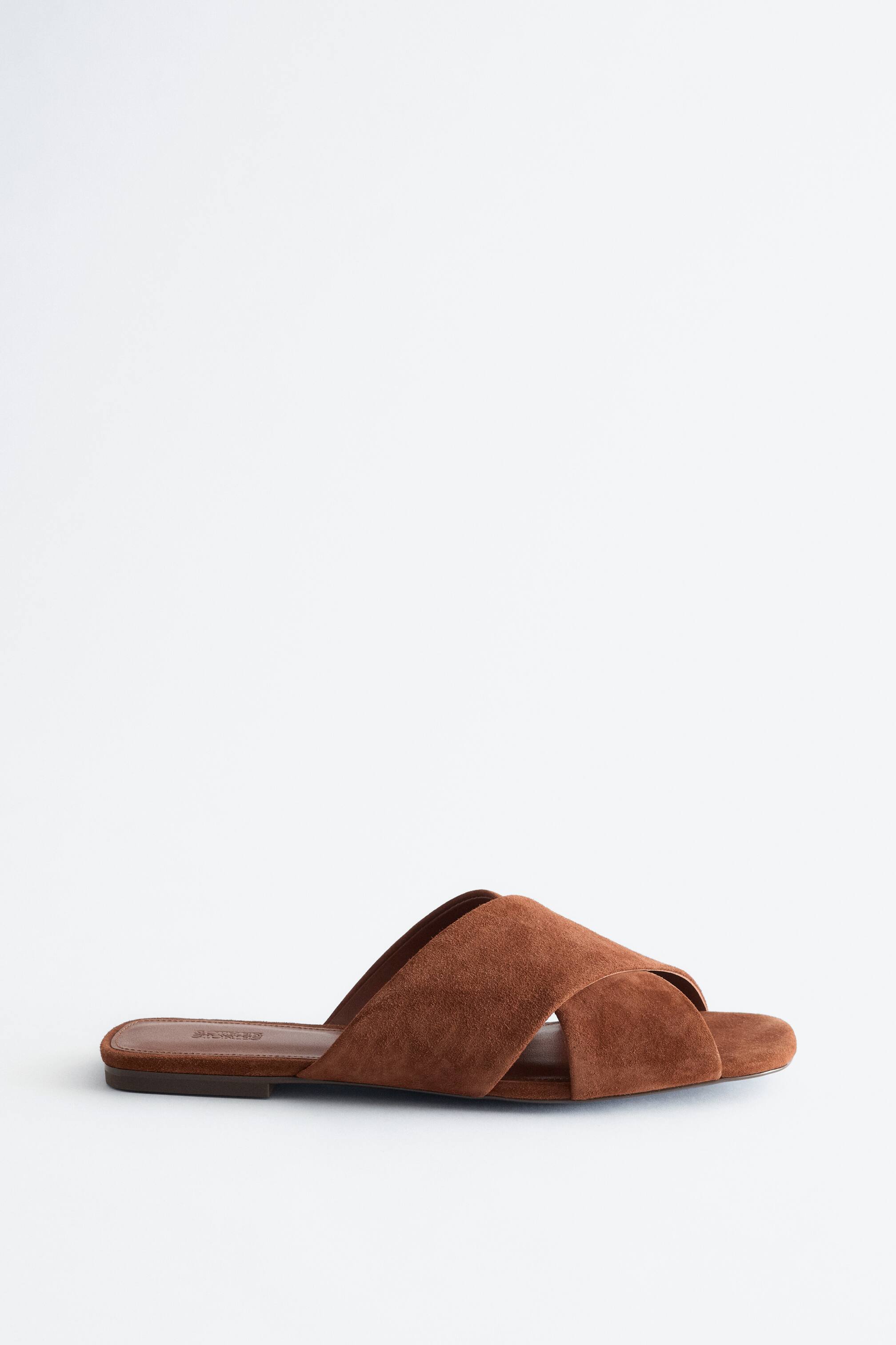 Näytä suurempi kuva: Ruskea mokkatohveli on käännetty vasemmalle, ja siinä on ristikkäiset hihnat päällä sekä tasainen ruskea pohja.