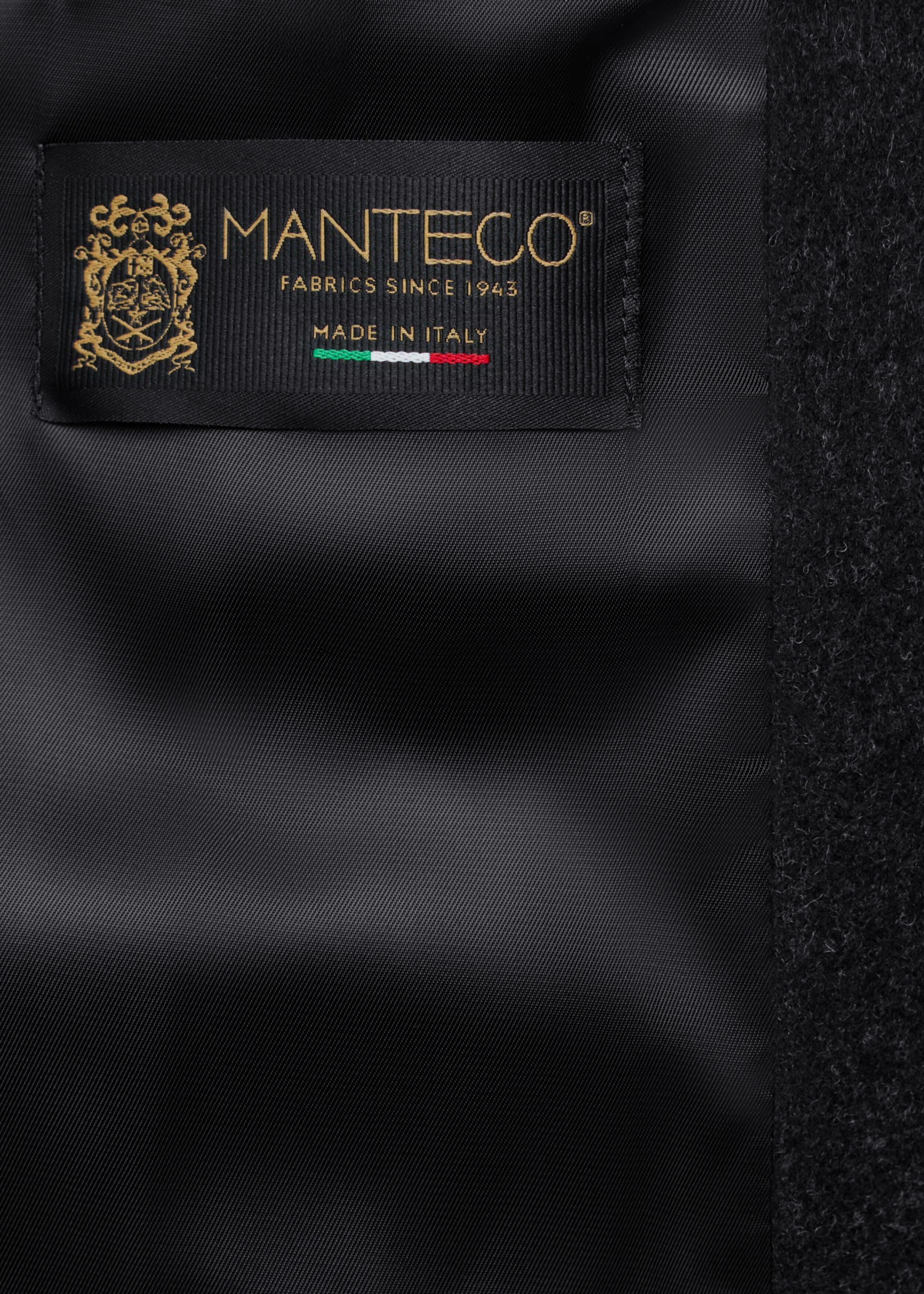 The coat’s smooth black lining displays a rectangular woven label stitched beside a textured dark wool edge. The label features gold-embroidered text reading “MANTECO,” “FABRICS SINCE 1943,” and “MADE IN ITALY”, accompanied by a small crest and an Italian flag motif.