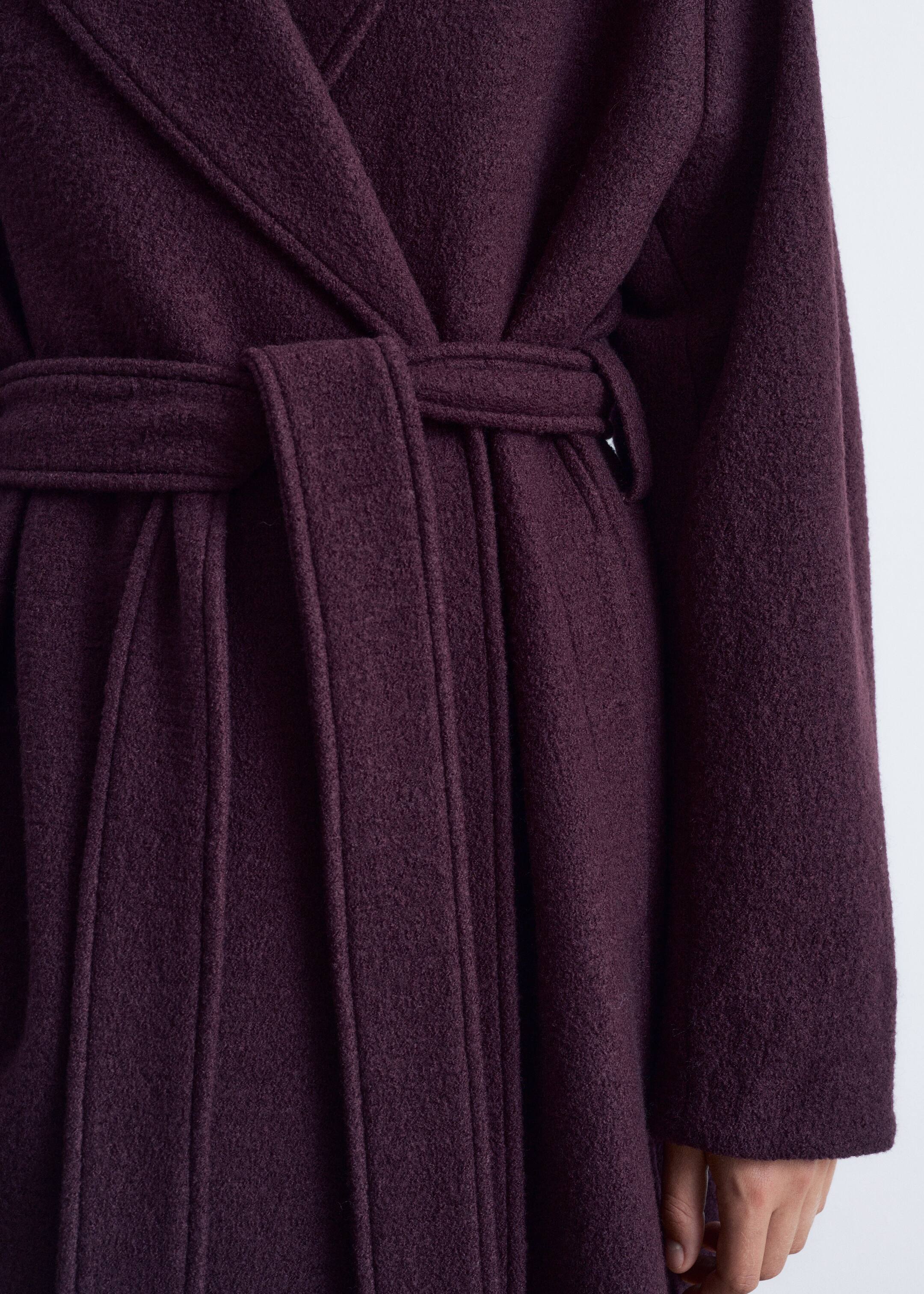 Agrandir l'image: Une vue rapprochée d'un manteau enveloppant violet foncé est présentée, avec une ceinture en tissu assorti nouée à la taille. Le manteau présente de larges revers et des plis fluides sous la ceinture, confectionné dans un tissu mélangé texturé en laine.